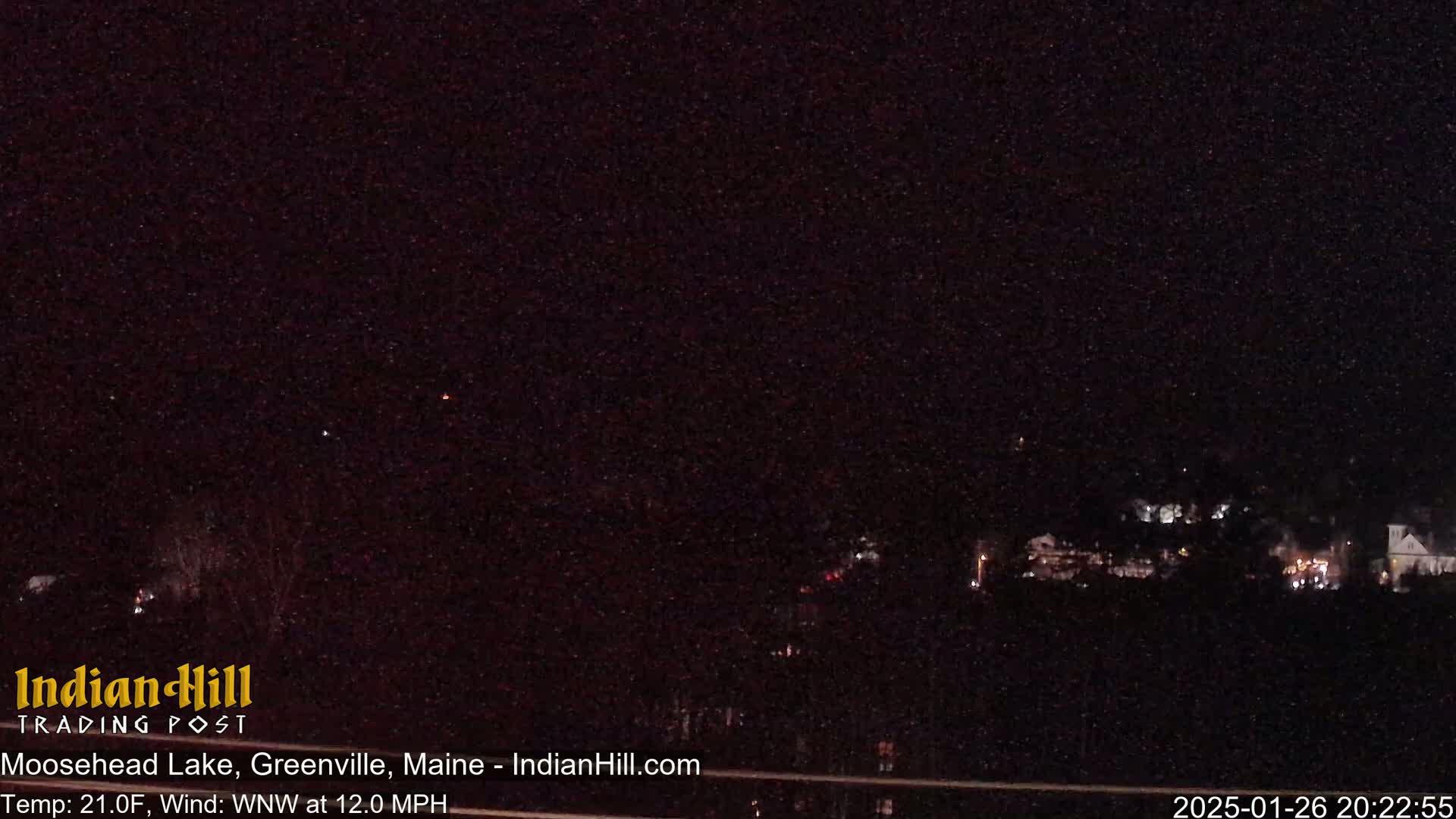 A nighttime long shot shows a dark, sparsely-lit landscape under a clear, starry sky with a northwest wind blowing at 12 mph and a temperature of 21 degrees Fahrenheit.