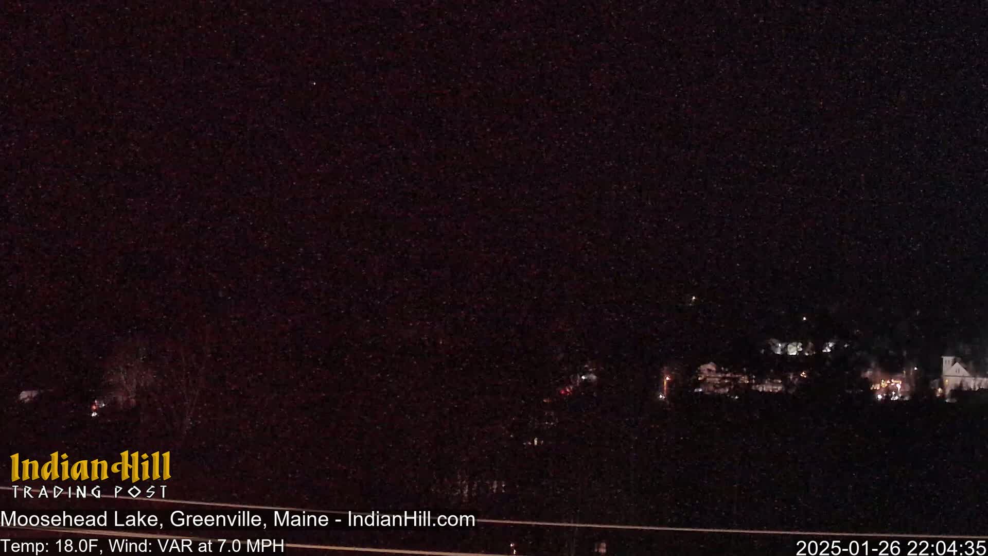 A nighttime long shot shows a dark, sparsely lit lakeside town under a clear, starry sky.