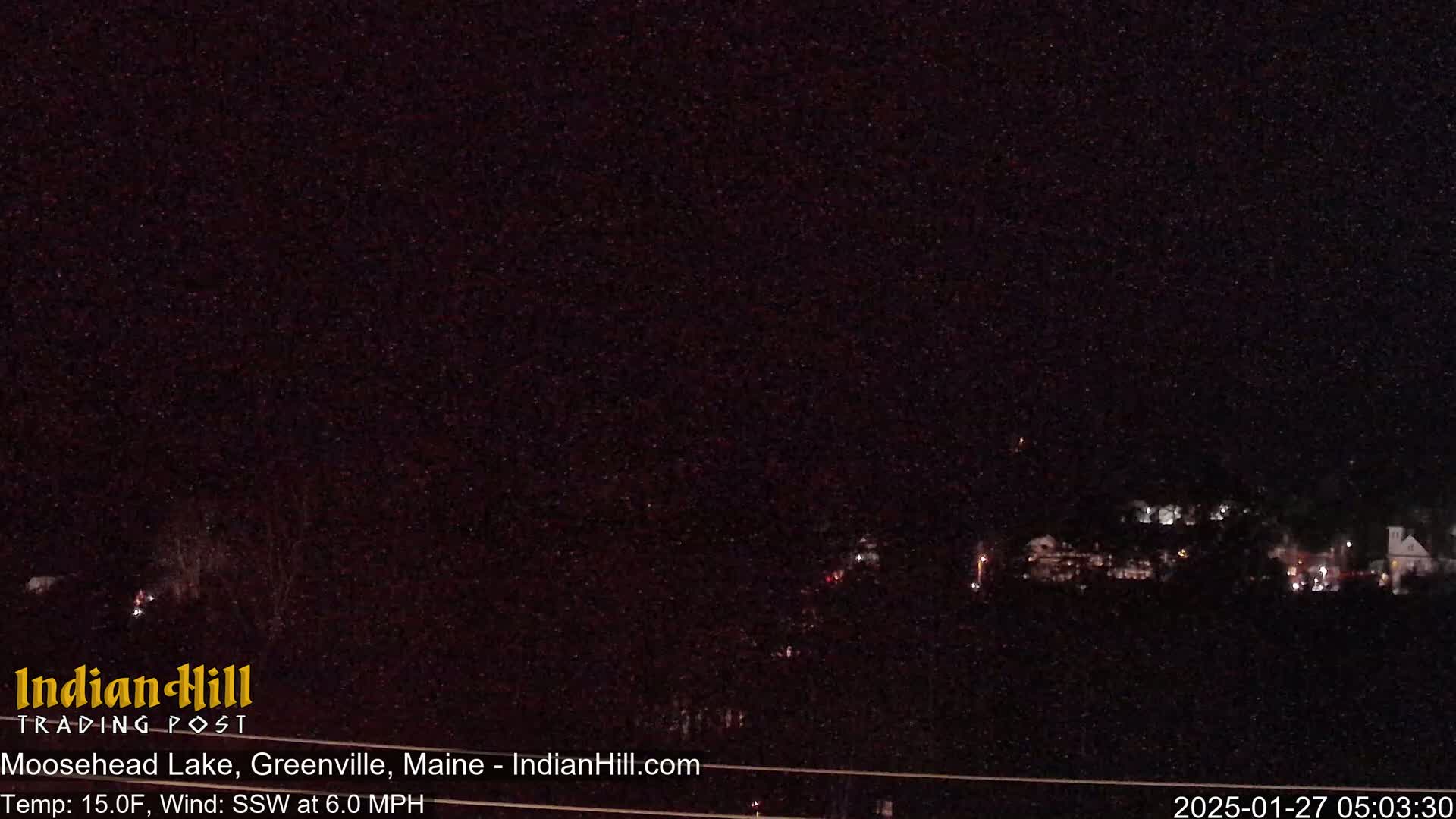 A nighttime, long shot of a dark landscape with a few distant lights, under a clear, starry sky with a temperature of 15 degrees Fahrenheit and a south-southwest wind.