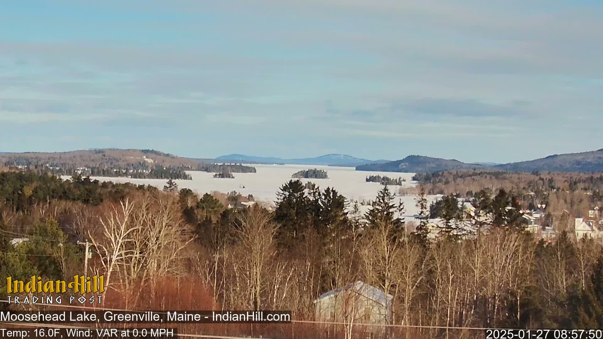 A snow-covered lake stretches into the distance, surrounded by snow-dusted trees and mountains under a clear, bright sky.