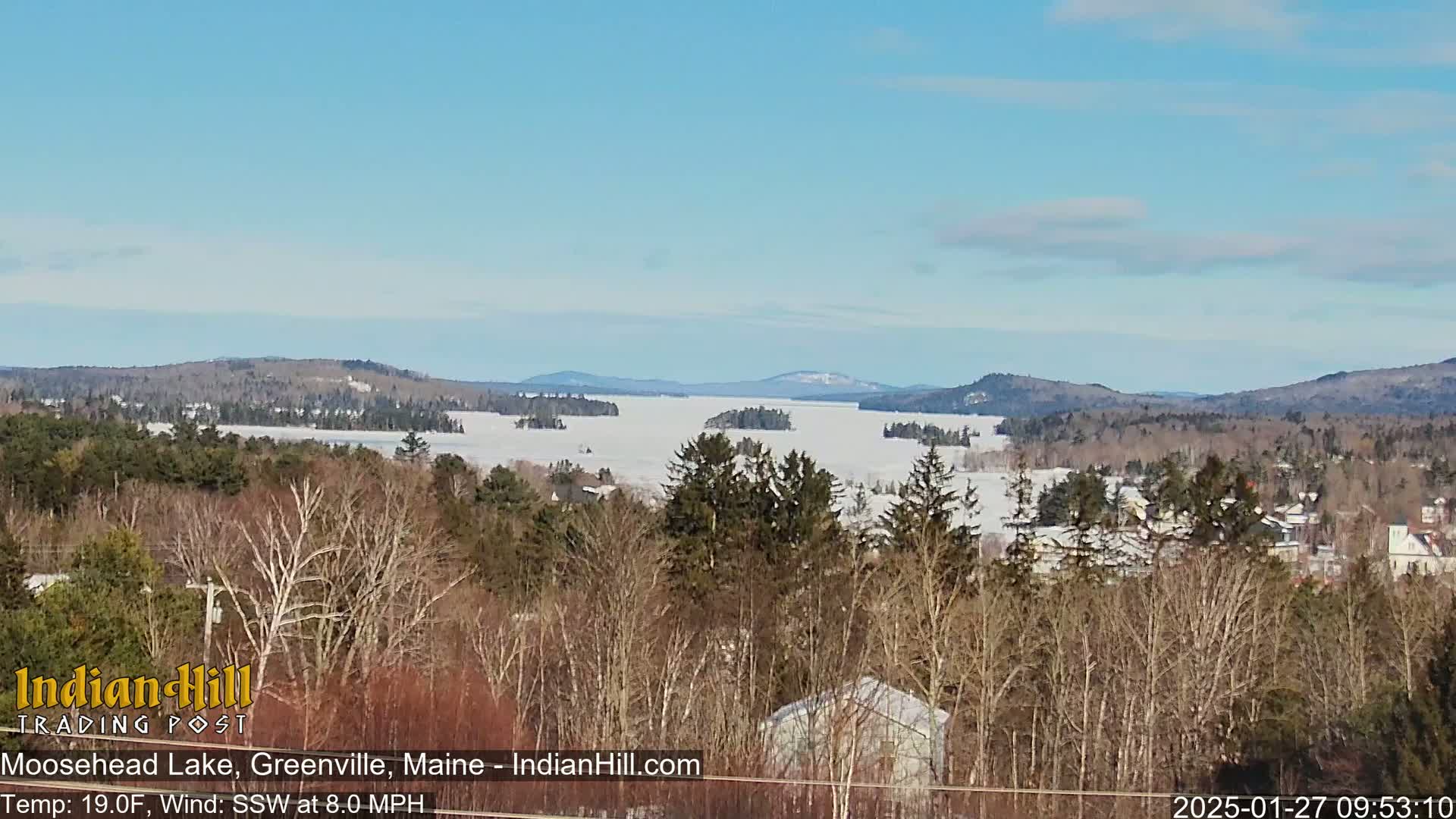 A snow-covered lake is visible from a vantage point overlooking a snow-dusted forest under a clear, bright sky.