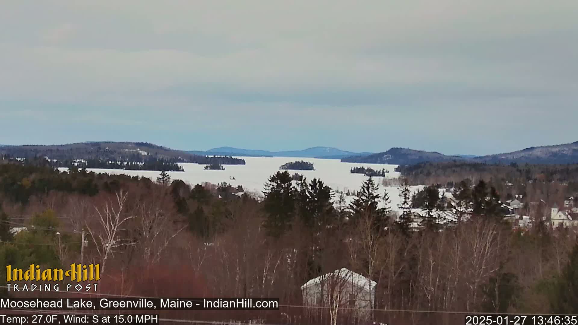 A snow-covered lake stretches to distant snow-dusted mountains under a cloudy sky.