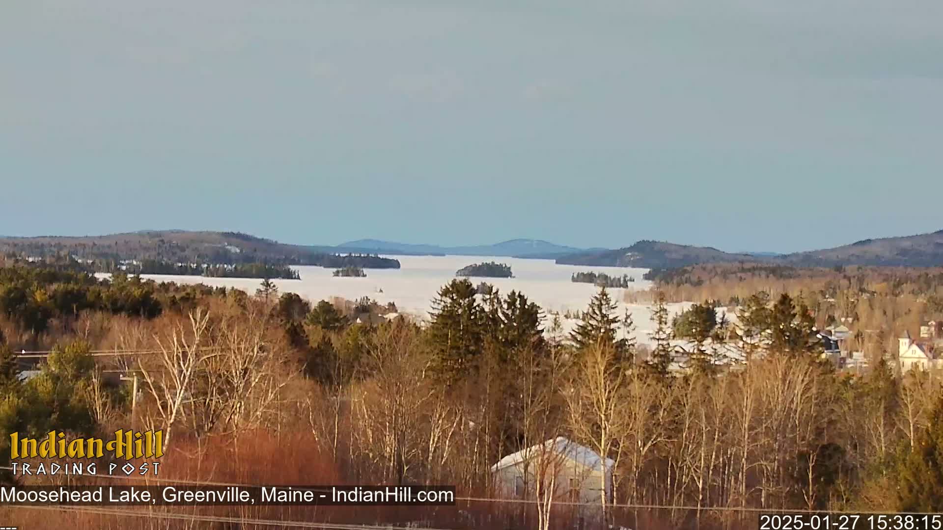 A snow-covered lake stretches out to distant, forested hills under a clear, bright sky.
