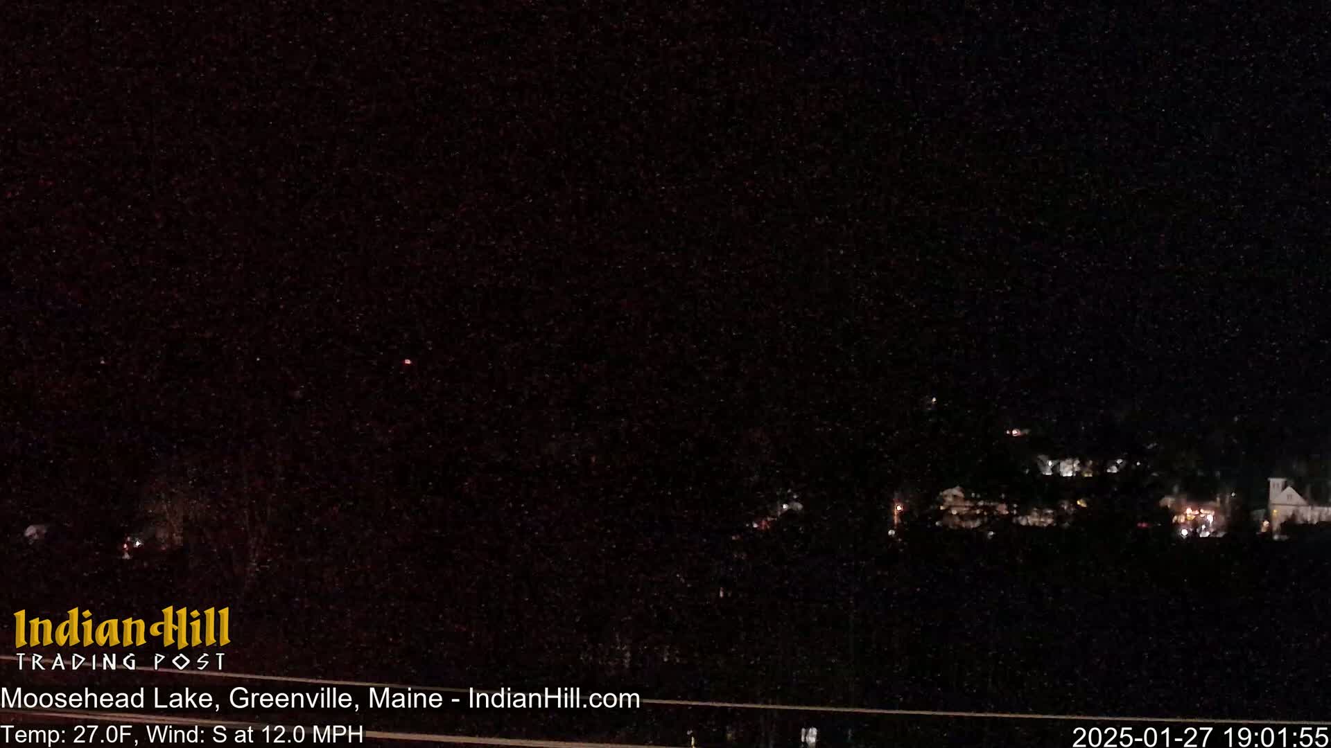 A nighttime long shot shows a distant town with faint lights under a dark, slightly snowy sky.
