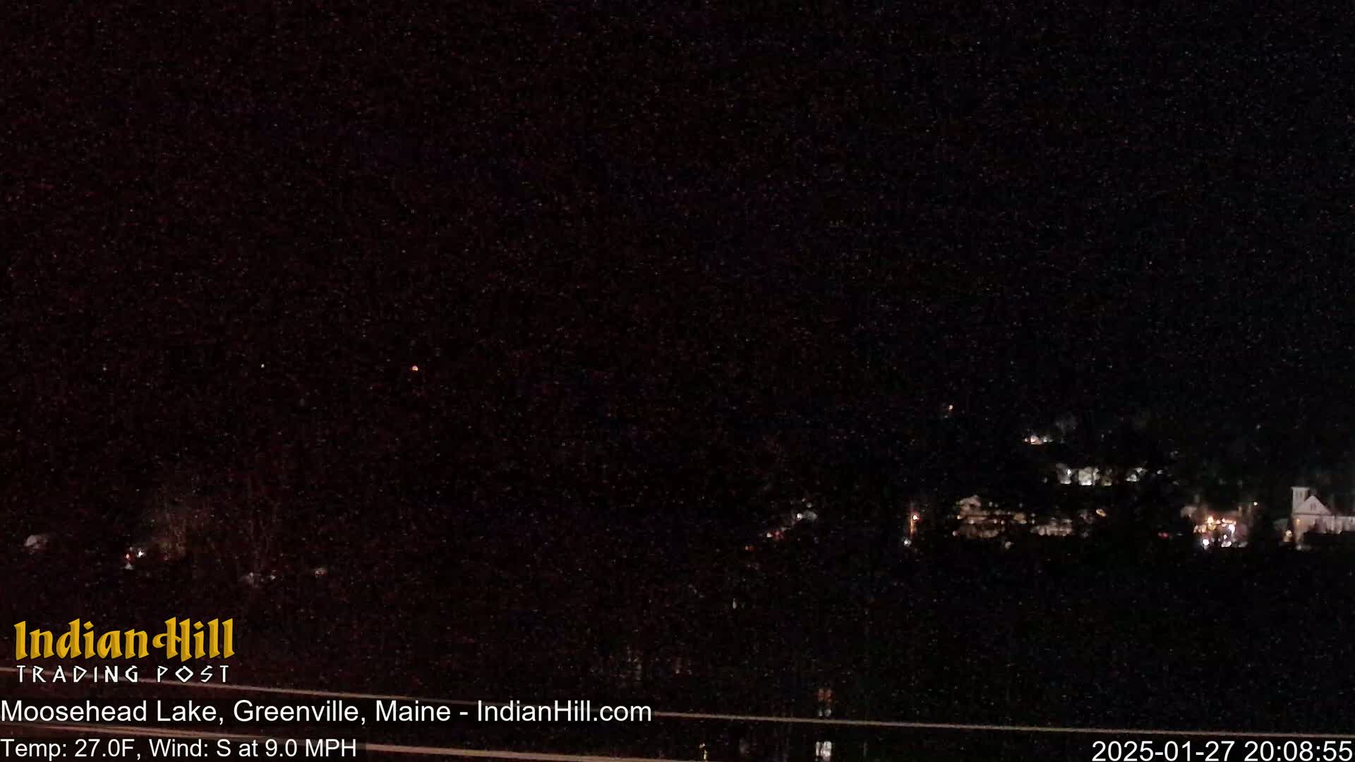 A nighttime long shot of a dark landscape with a few distant lights, under a clear, starry sky, with a south wind.