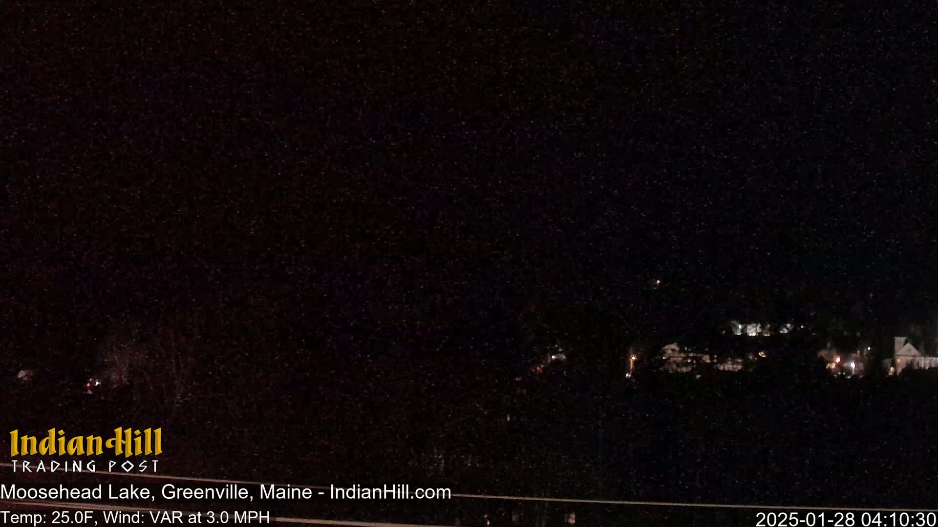 A dark, nighttime scene shows a few faint lights in the distance under a snow-filled sky.