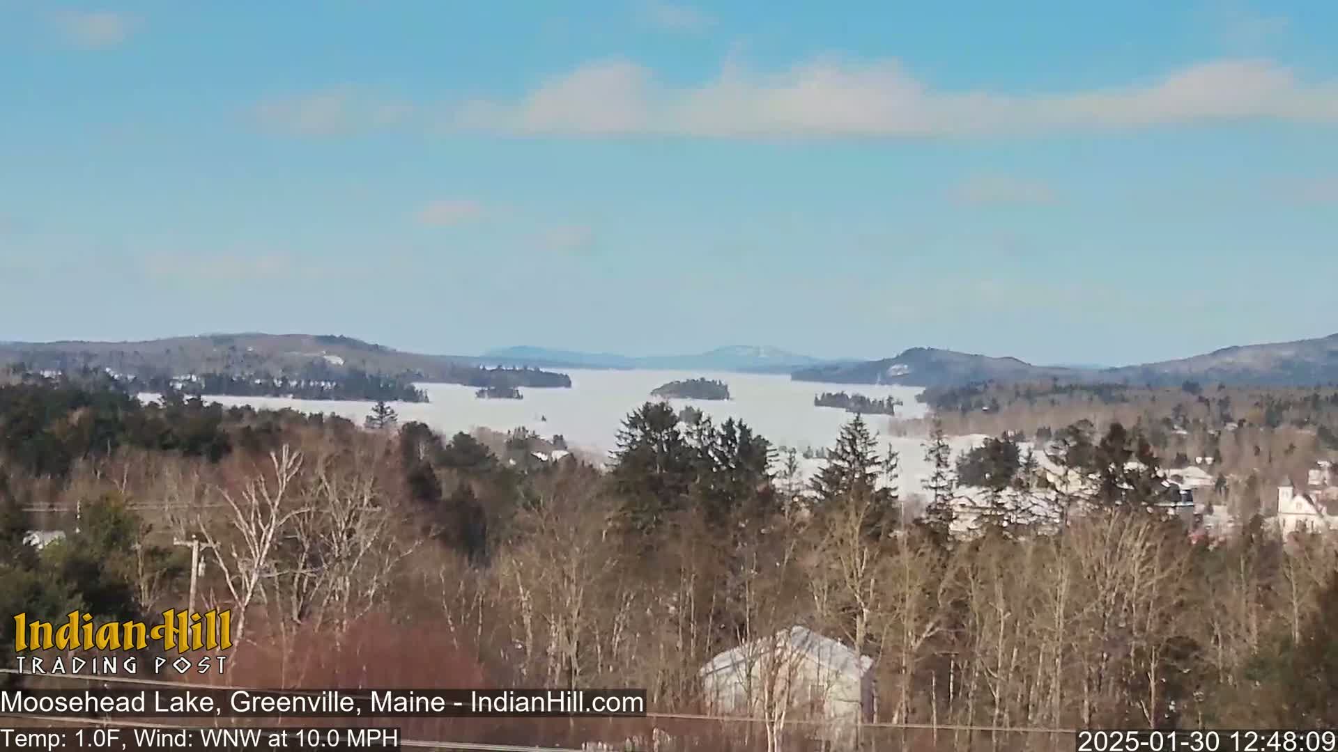 A partly frozen lake is visible from a hilltop on a clear, sunny day with a light wind.