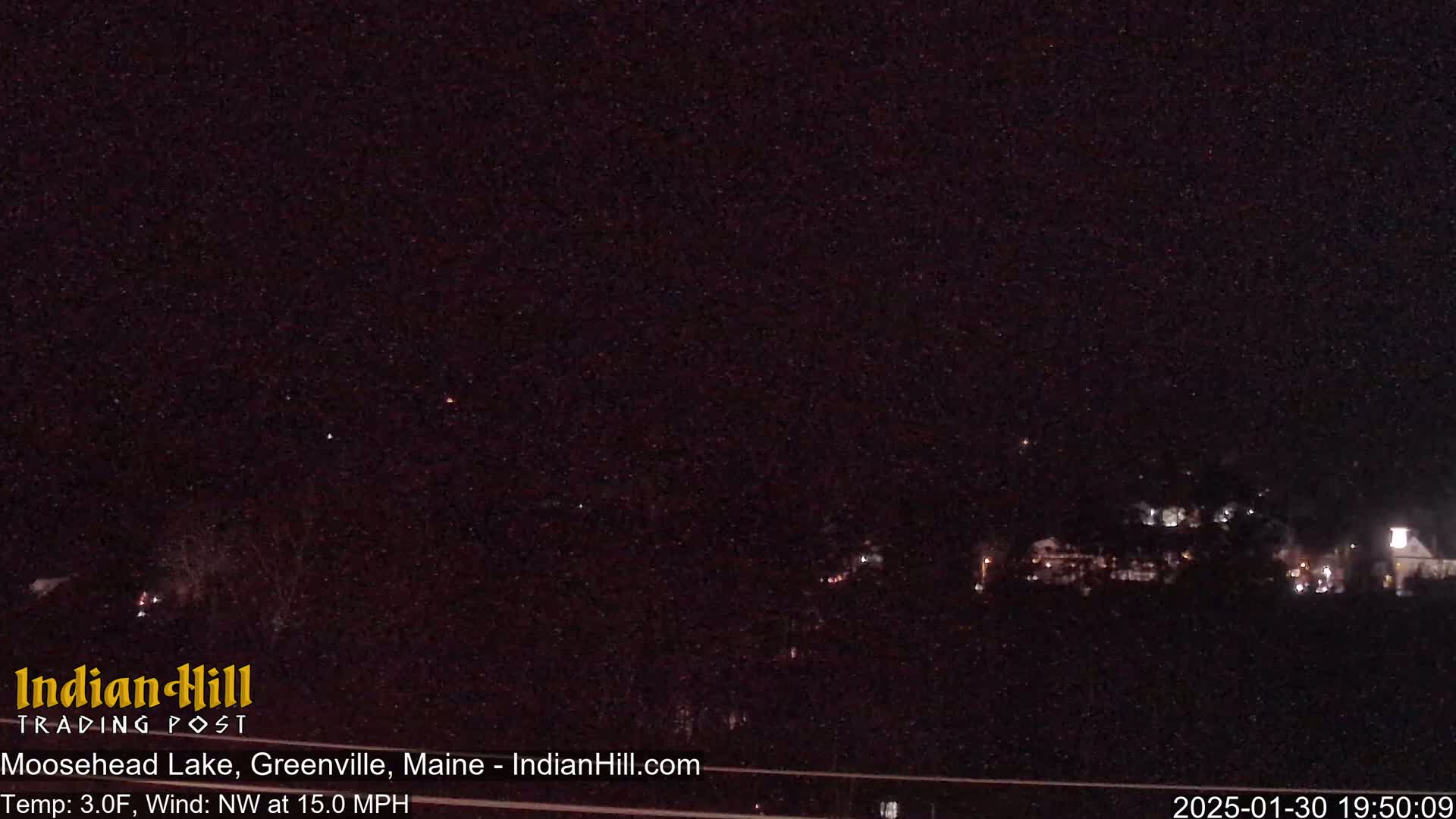 A nighttime long shot of a dark landscape with a few distant lights, under a clear, dark sky with a northwest wind at 15 mph and a temperature of 3 degrees Fahrenheit.