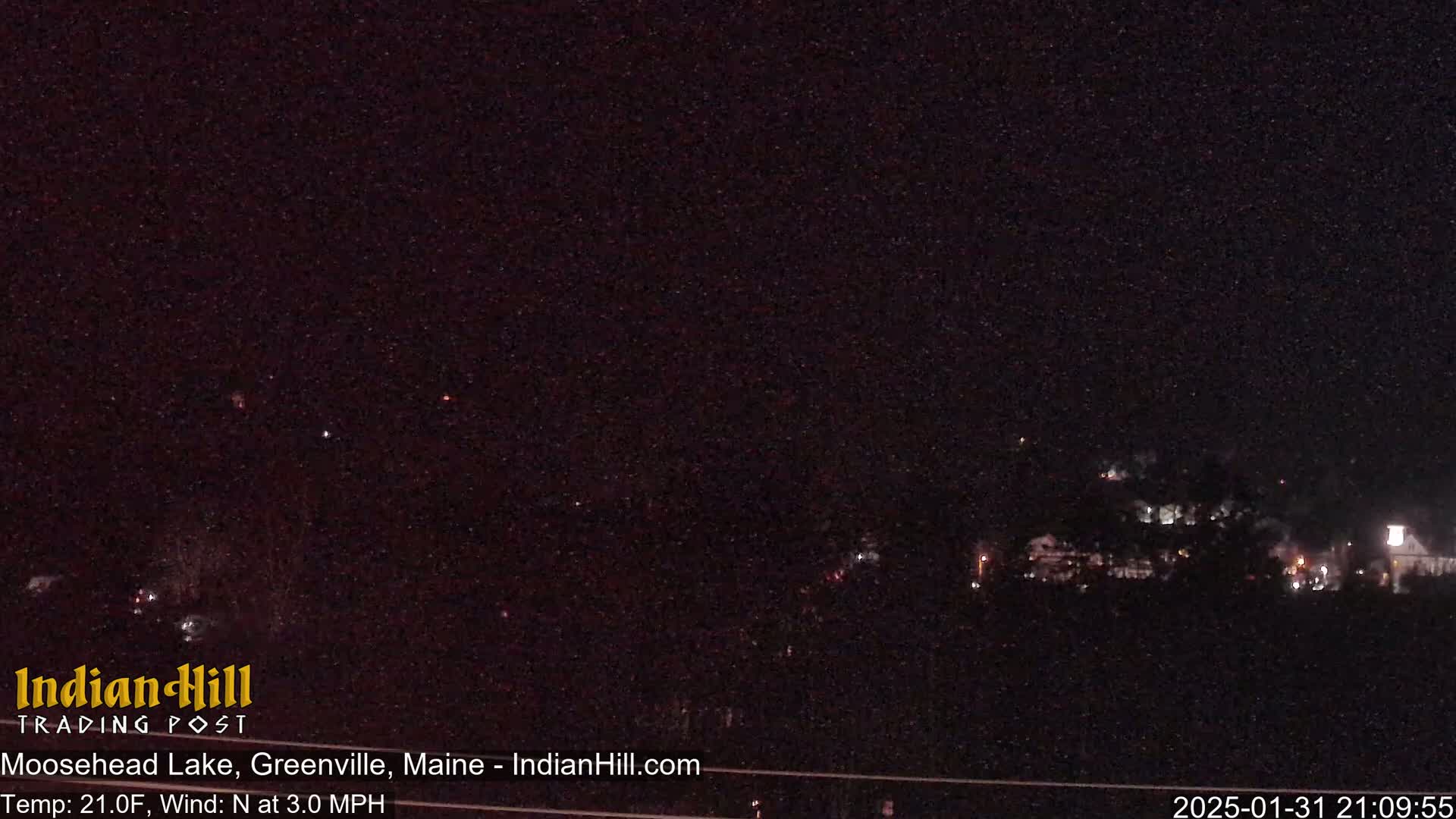 A nighttime view of dimly lit buildings and trees under a dark, starry sky with a temperature of 21 degrees Fahrenheit and a north wind at 3 mph.
