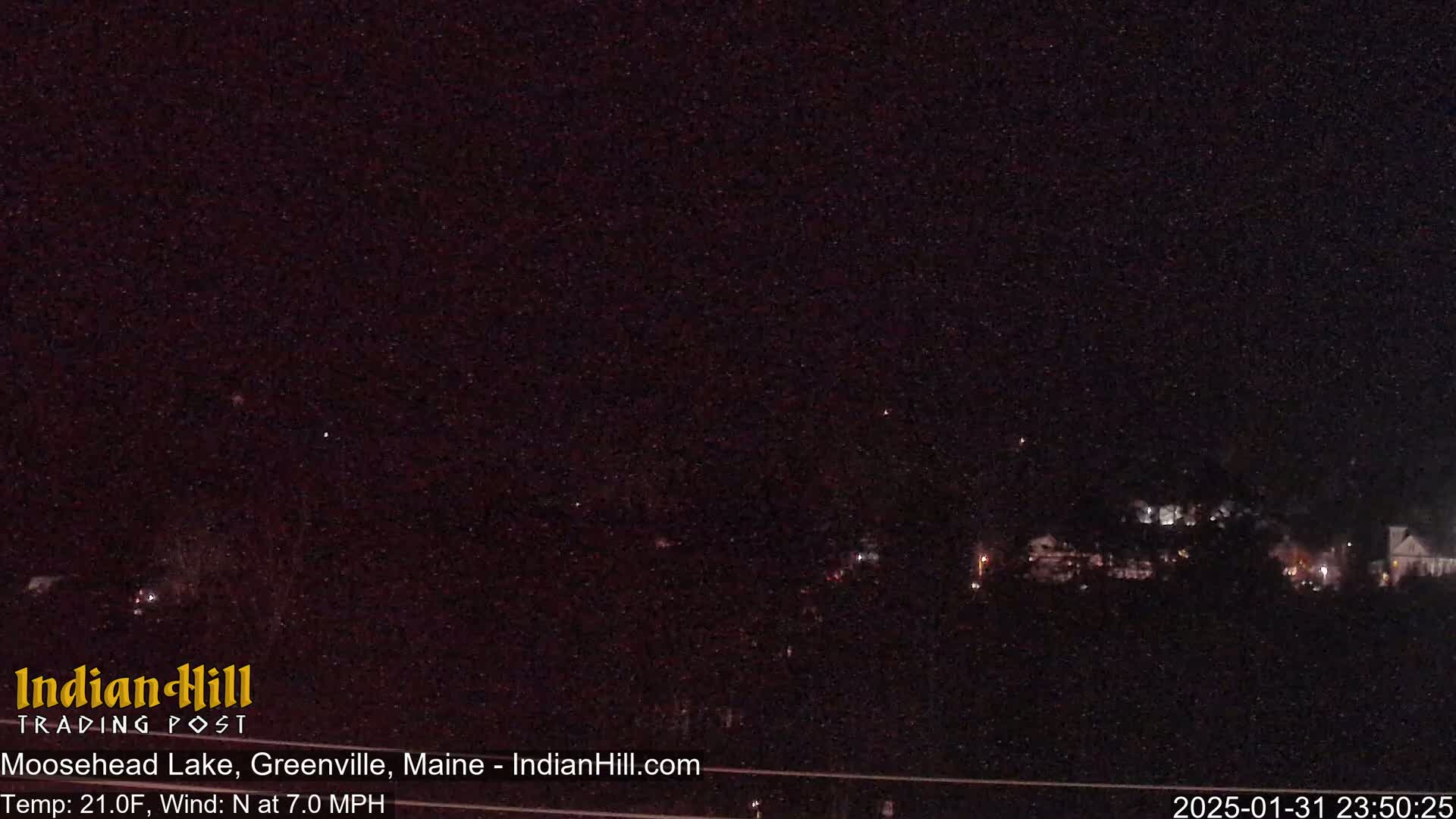 A nighttime long shot of a dark landscape with a few distant lights, under a mostly clear, dark sky.