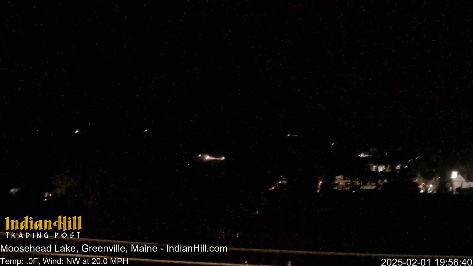 A nighttime long shot shows a dark landscape with a few distant lights under a dark, starry sky with a northwest wind blowing at 20 mph.