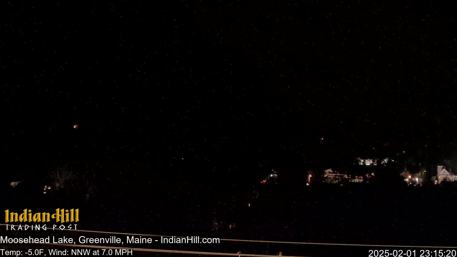 A nighttime, snowless outdoor scene shows a few distant lights in the darkness, under a mostly clear, star-filled sky.