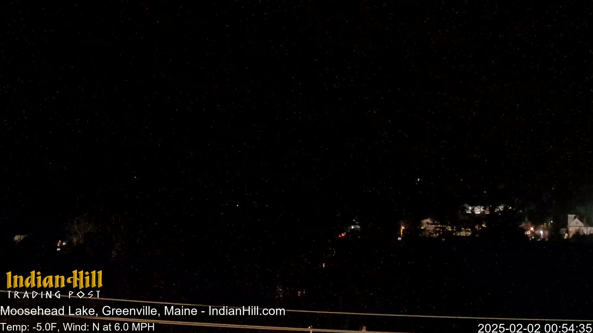 A nighttime, snowy scene shows a few distant lights in the darkness with a north wind at 6.0 mph and a temperature of -5.0°F.