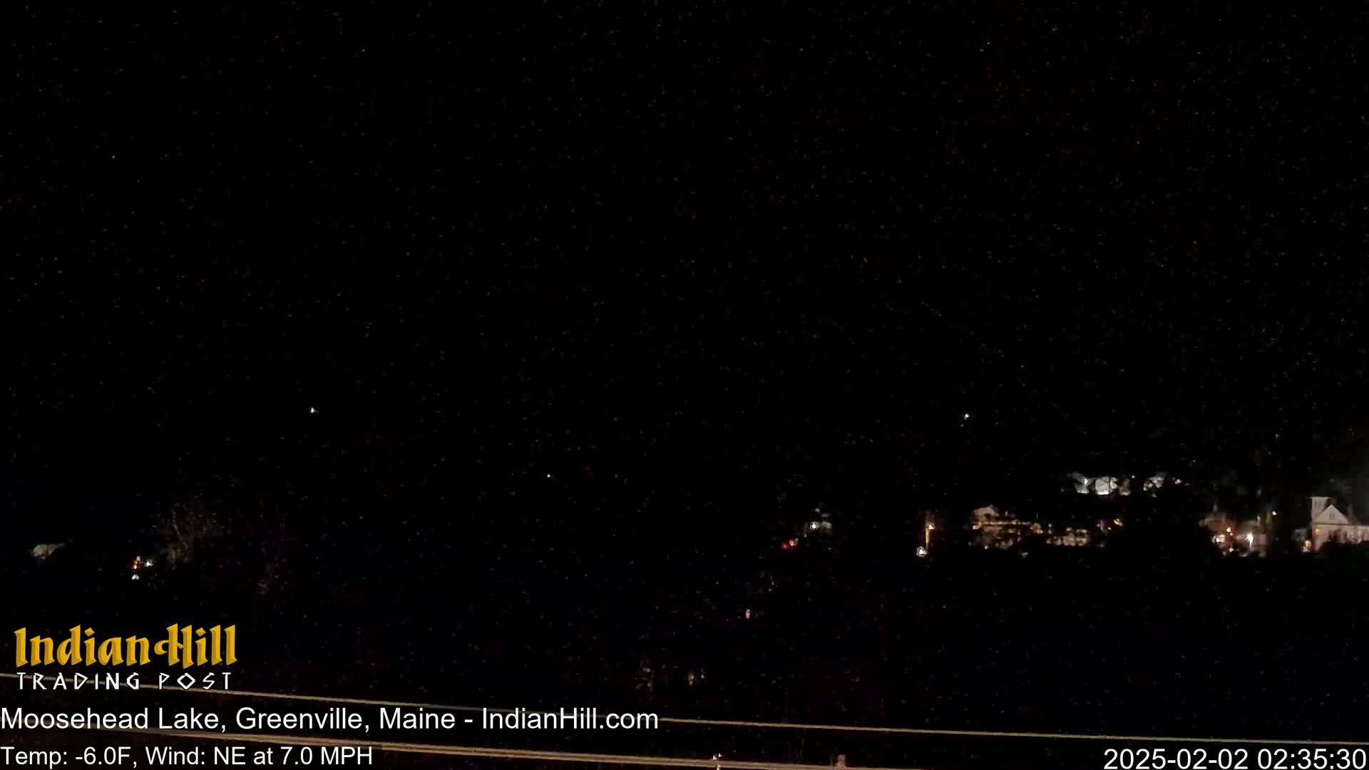 A nighttime long shot shows a dark landscape with sparsely lit buildings in the distance under a dark, snowy sky.