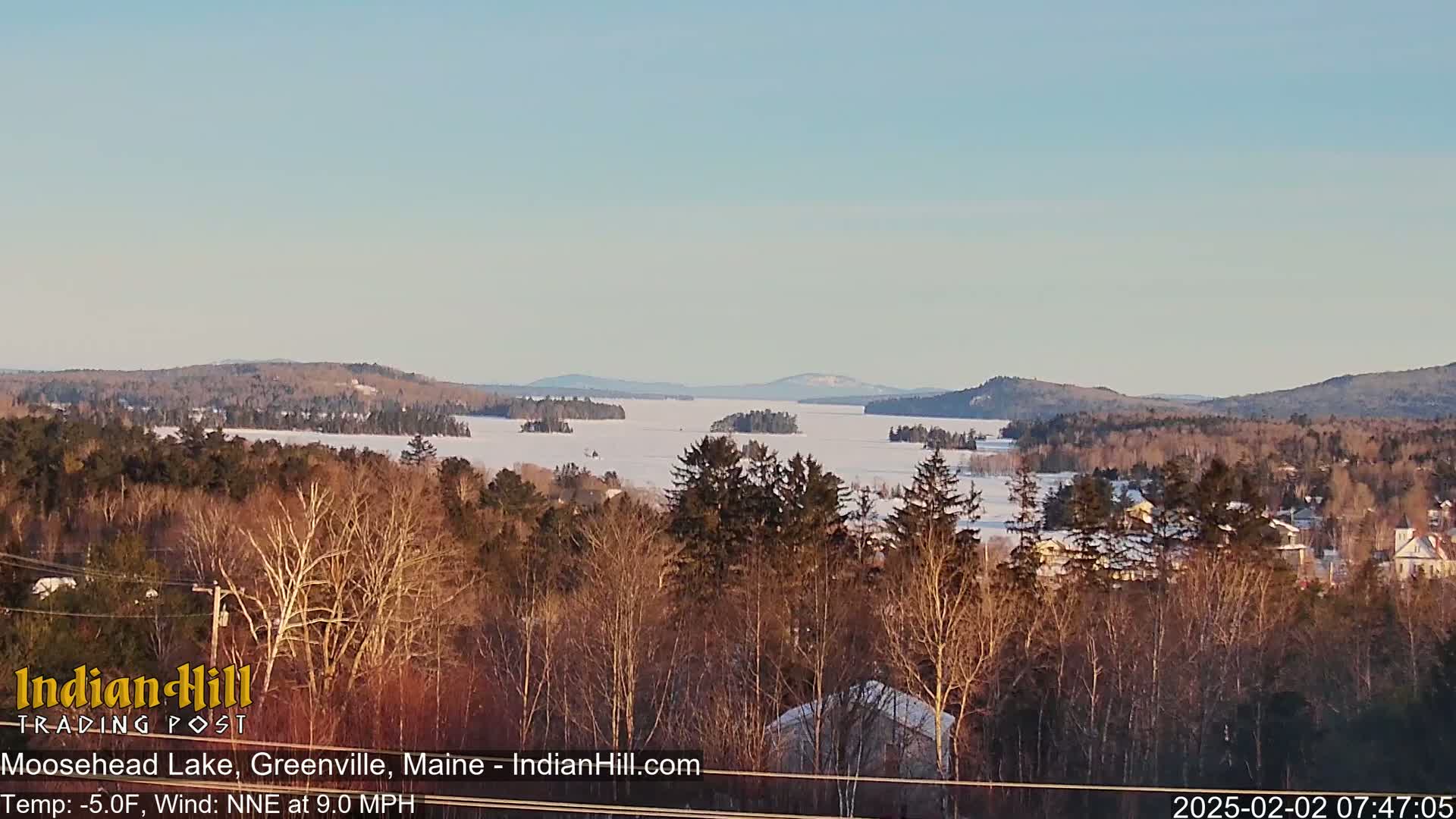 A snow-covered lake stretches to distant mountains under a clear, light-blue sky.