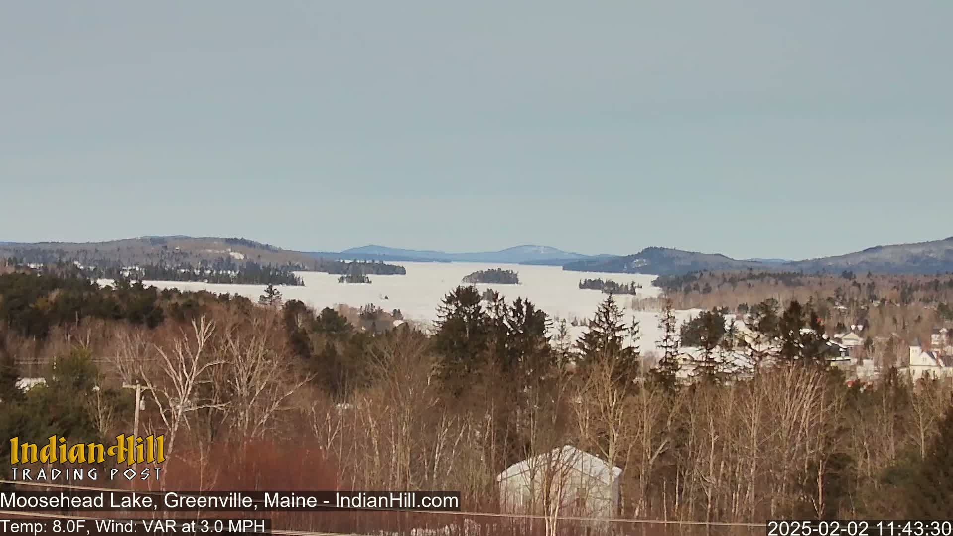A snow-covered lake stretches to distant hills under a clear, light-grey sky.
