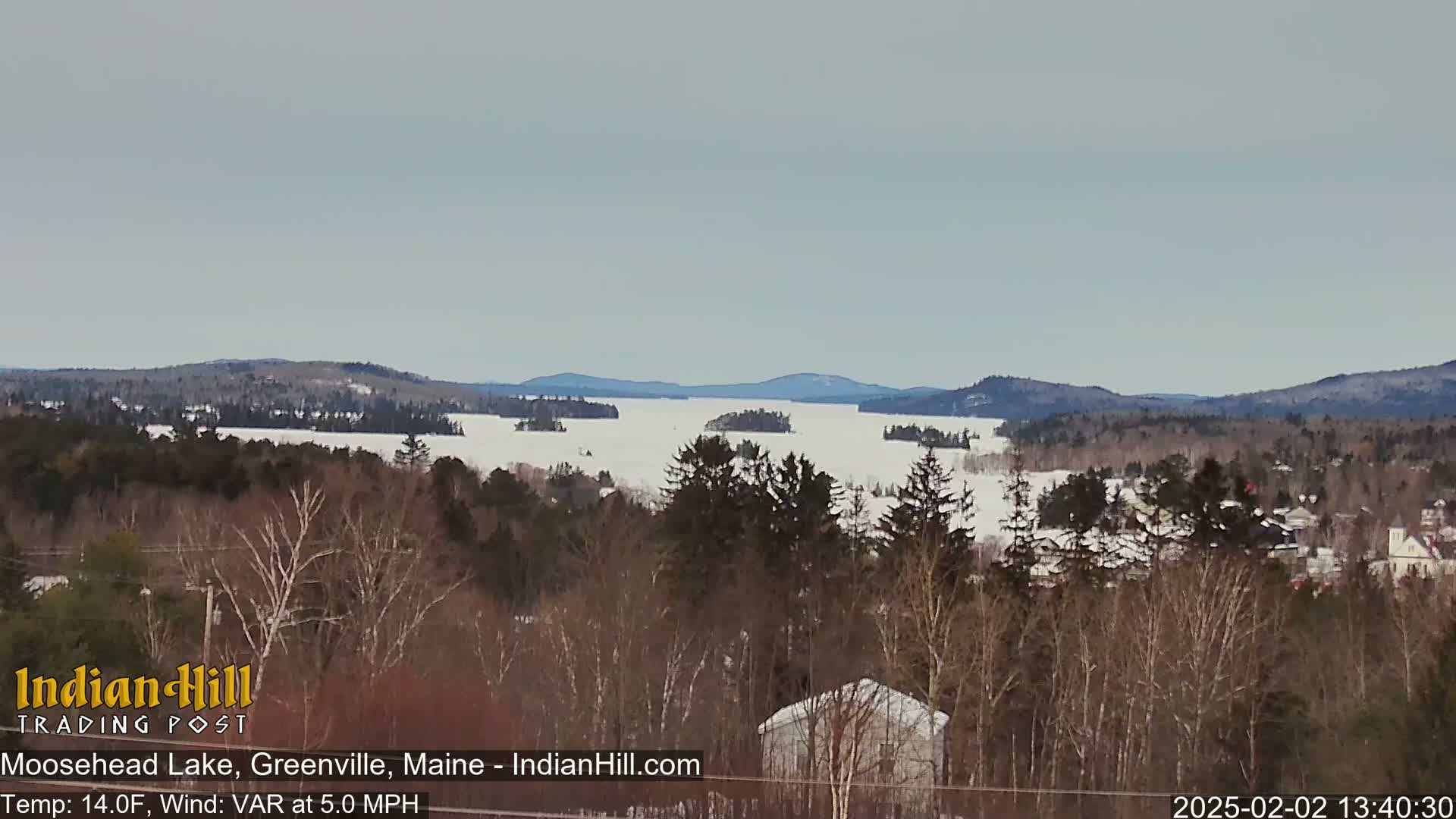 A snow-covered lake stretches to distant, snow-dusted hills under a cloudy sky.