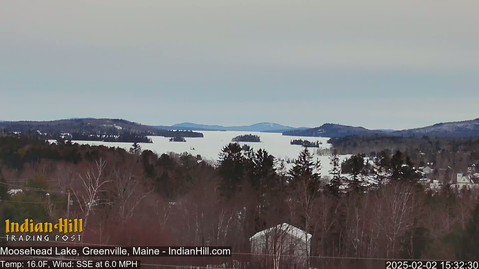 A snow-covered lake with several small islands is viewed from a distance, under a mostly cloudy sky.