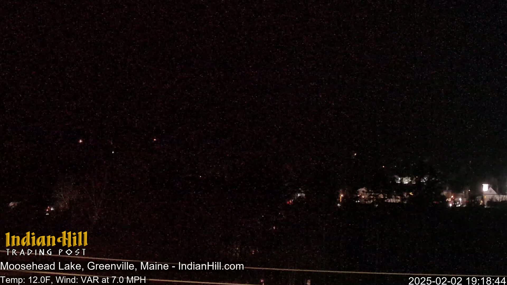 A nighttime long shot of a sparsely lit landscape under a dark, starry sky with a variable wind at 7.0 mph and a temperature of 12 degrees Fahrenheit.