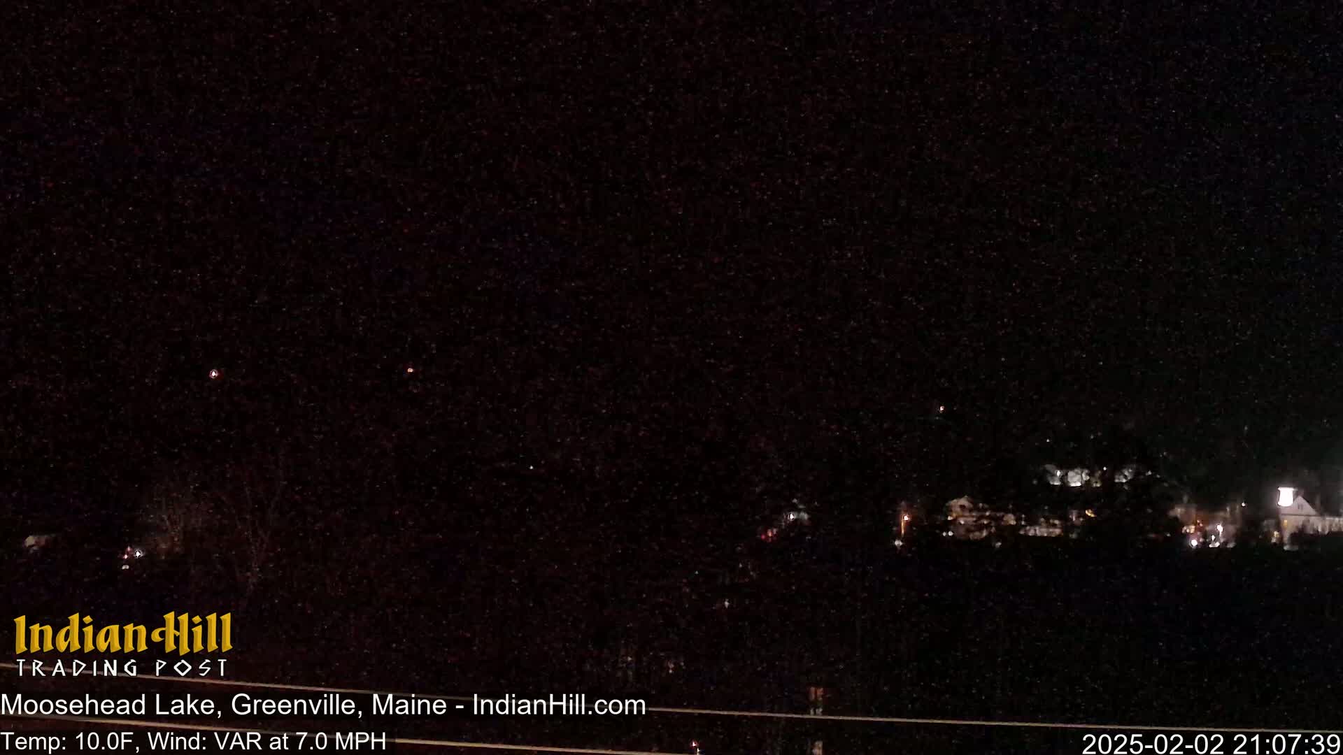 A nighttime long shot shows a dark landscape with a few faint lights in the distance under a dark, starry sky.