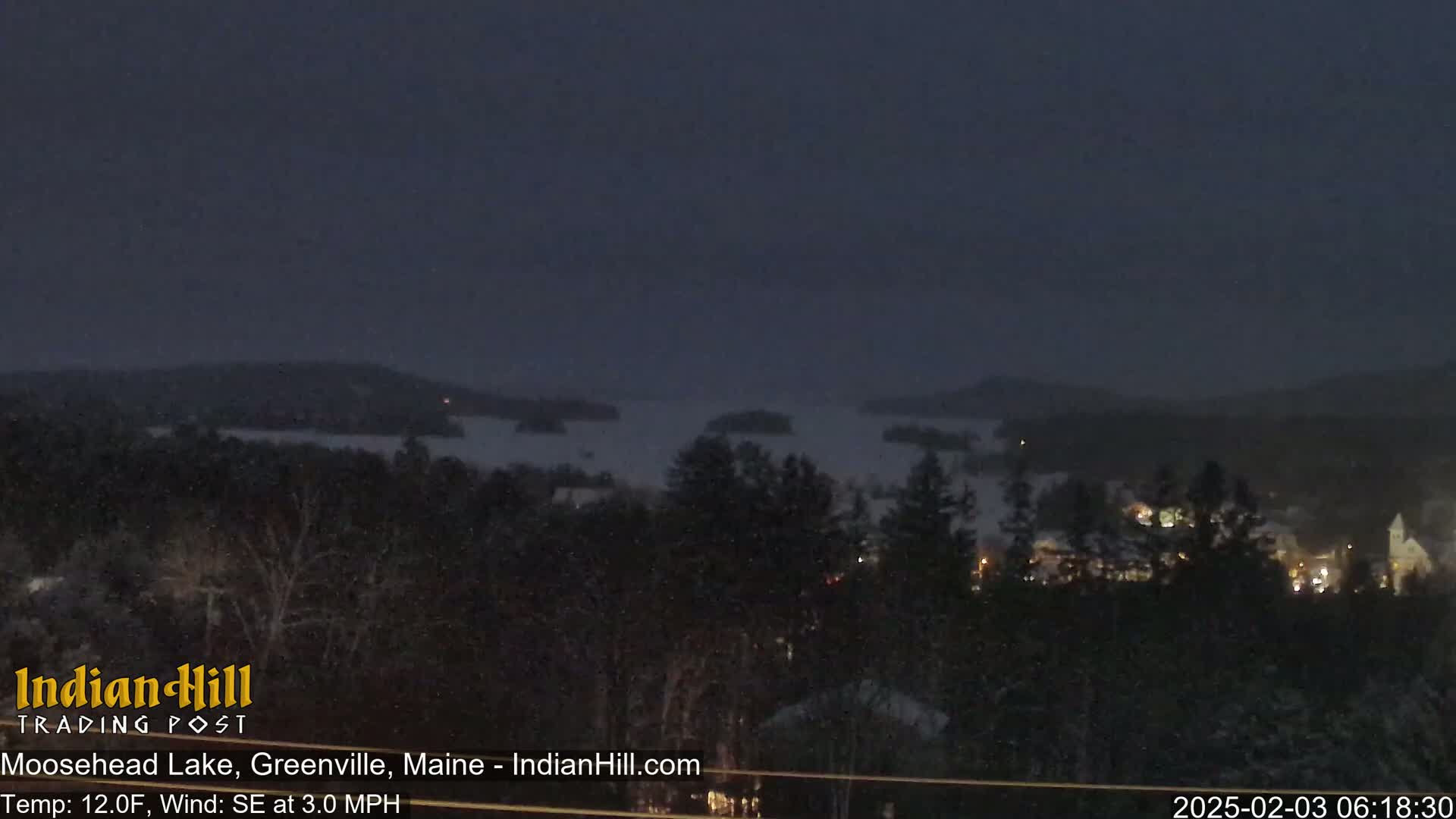 A nighttime view of a snow-covered landscape shows a lake with islands under a dark sky.