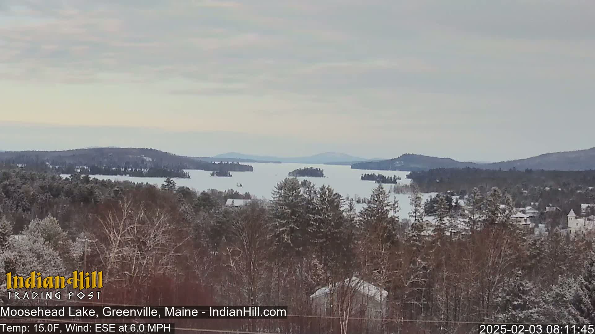 A snow-covered landscape overlooks a partially frozen lake with several islands, under a cloudy sky.