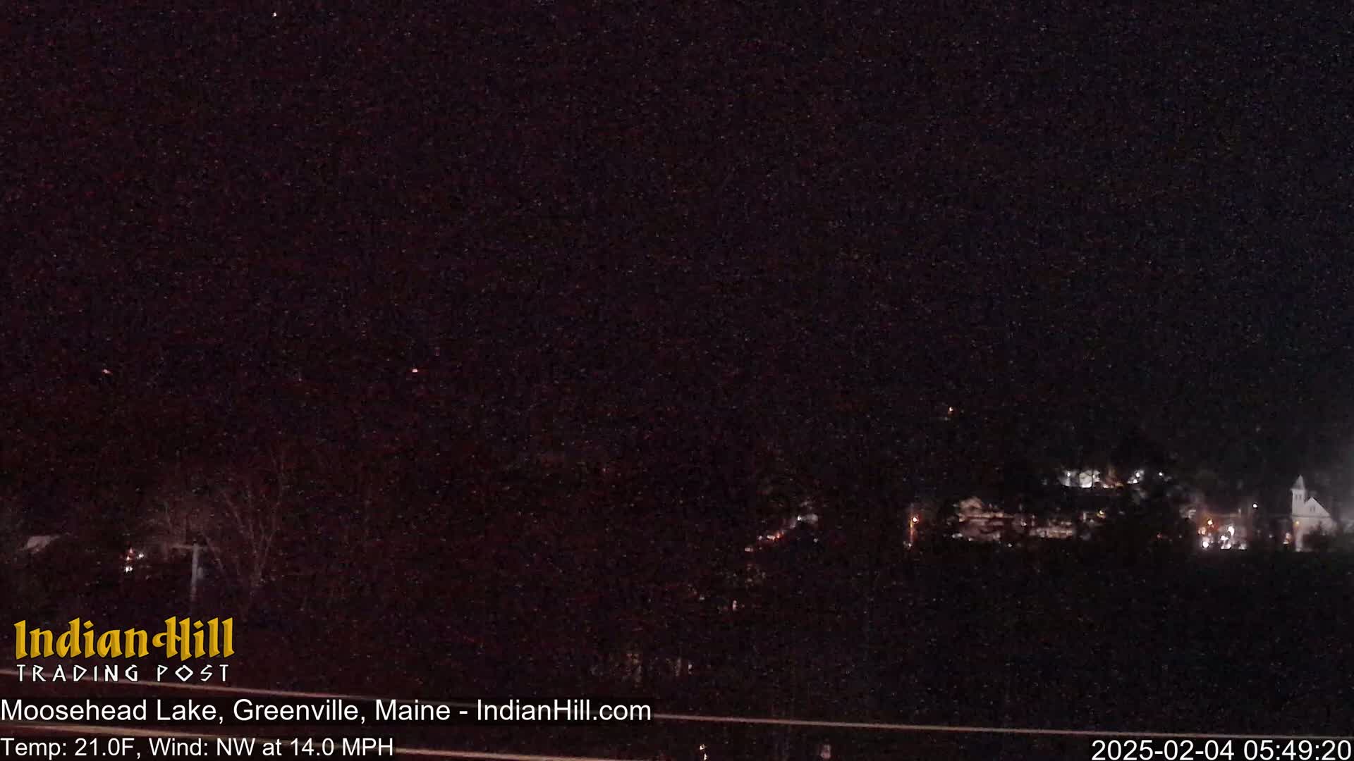 A nighttime long shot of a sparsely lit town under a dark, snow-filled sky with a northwest wind.