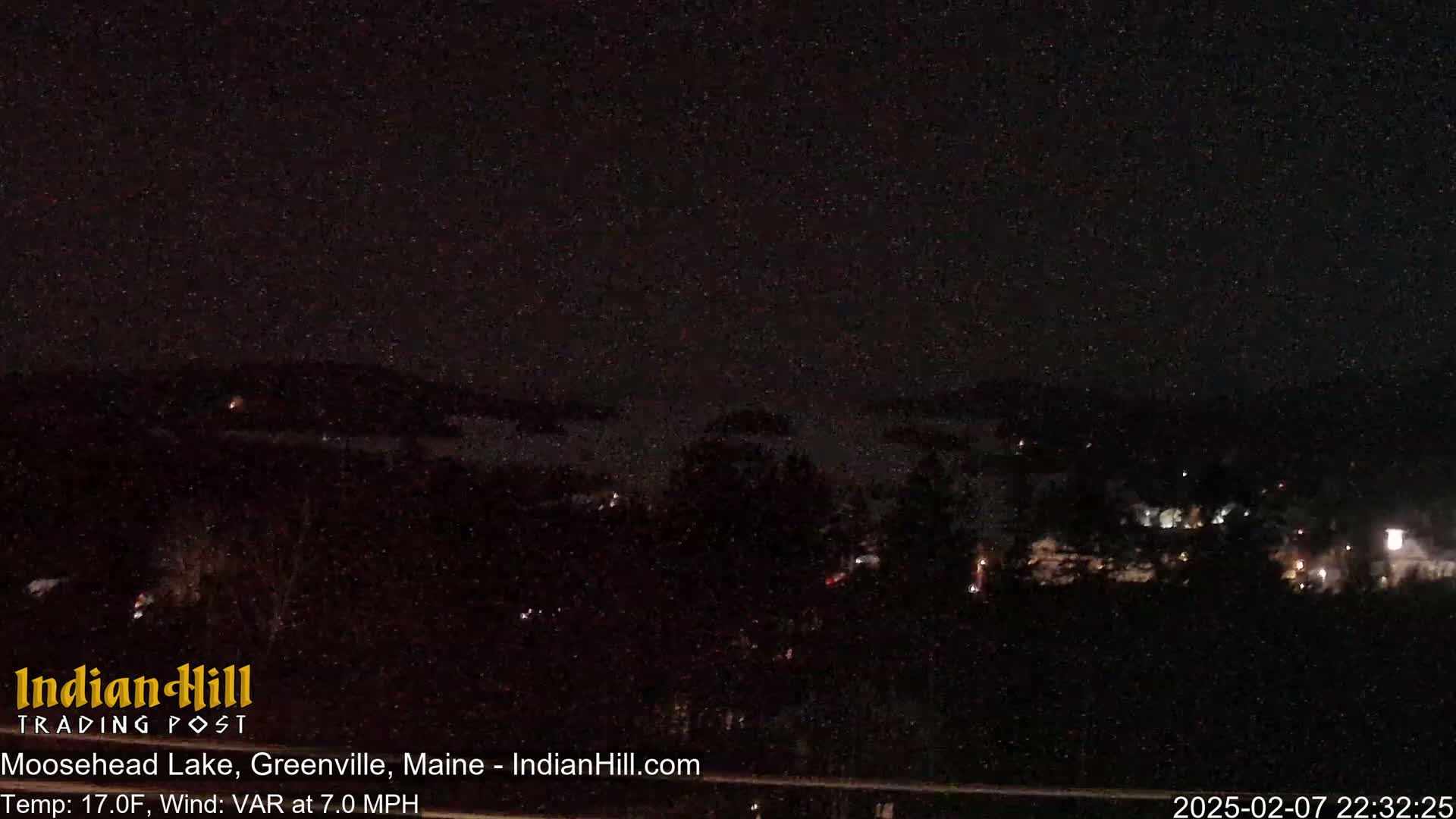 A nighttime, snowy scene shows a dark landscape with a few distant lights under a starlit sky.