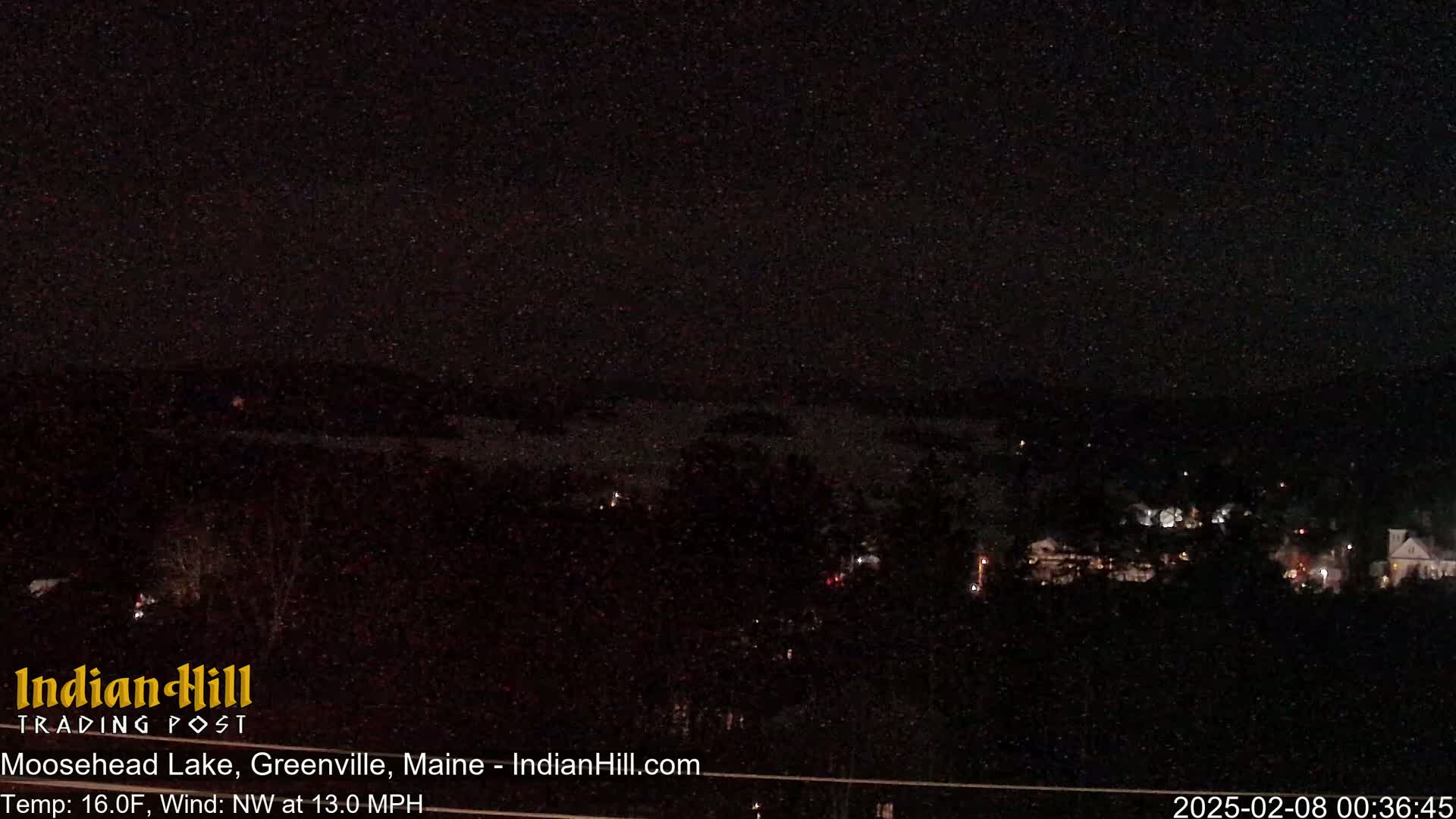 A nighttime long shot shows a dark body of water and a sparsely lit town under a clear, star-filled sky.