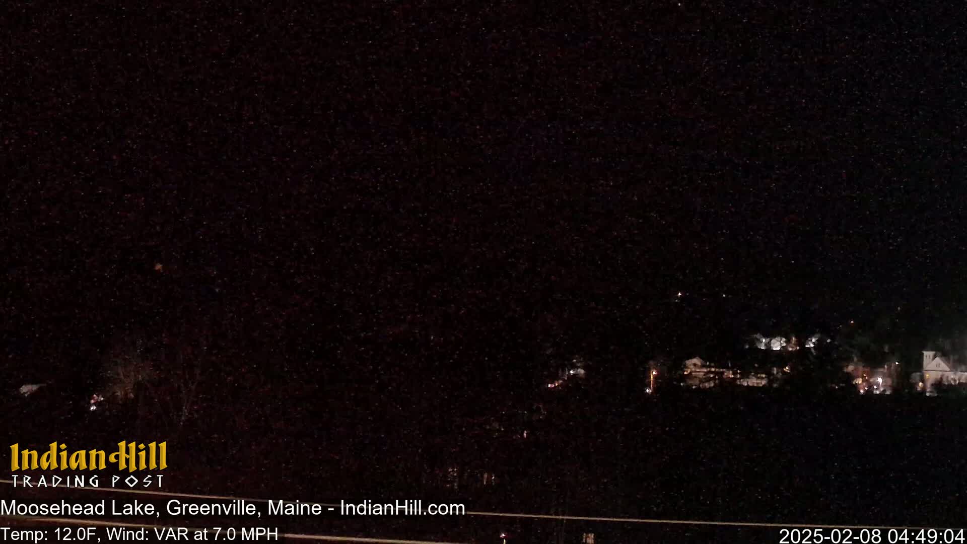 A nighttime long shot of a distant town with scattered lights under a clear, starry sky.