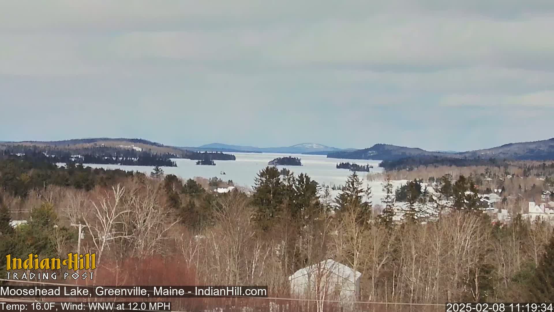 A partially frozen lake stretches to distant snow-covered hills under a cloudy sky.