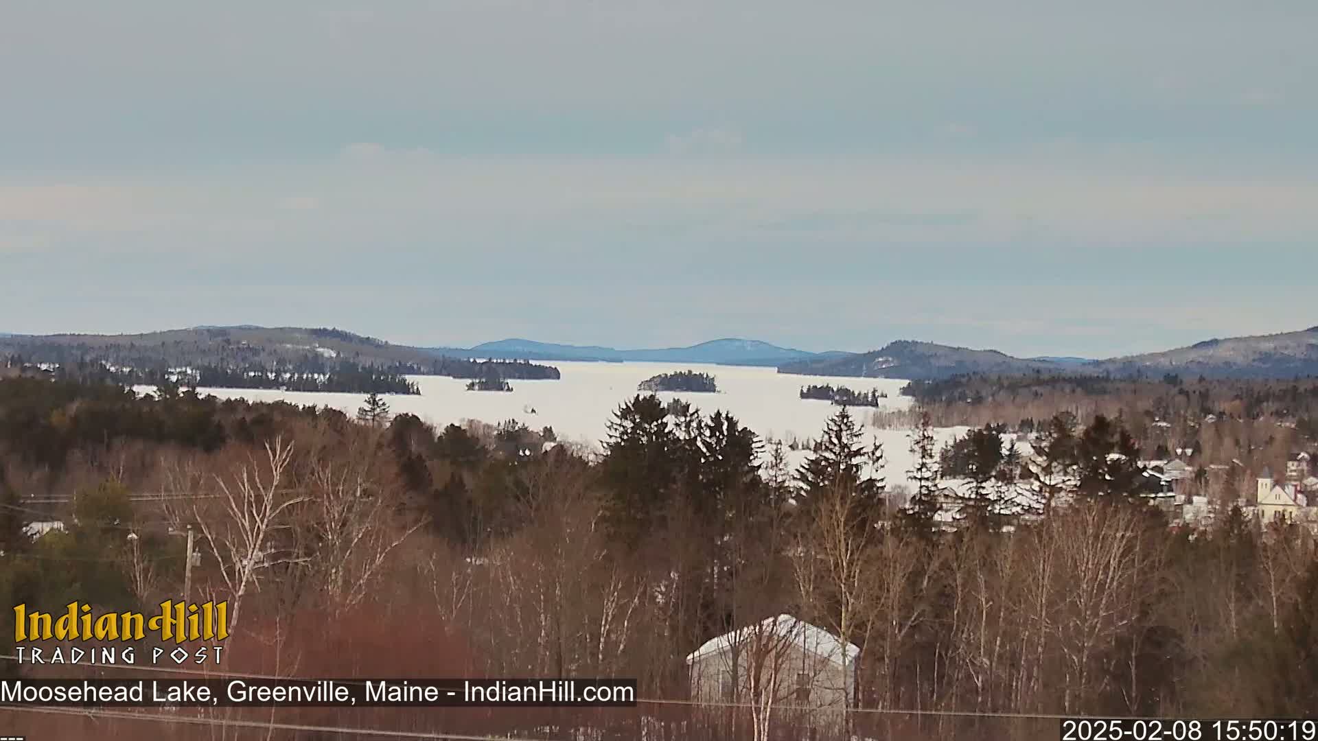 A snow-covered lake stretches to distant forested hills under a cloudy sky.