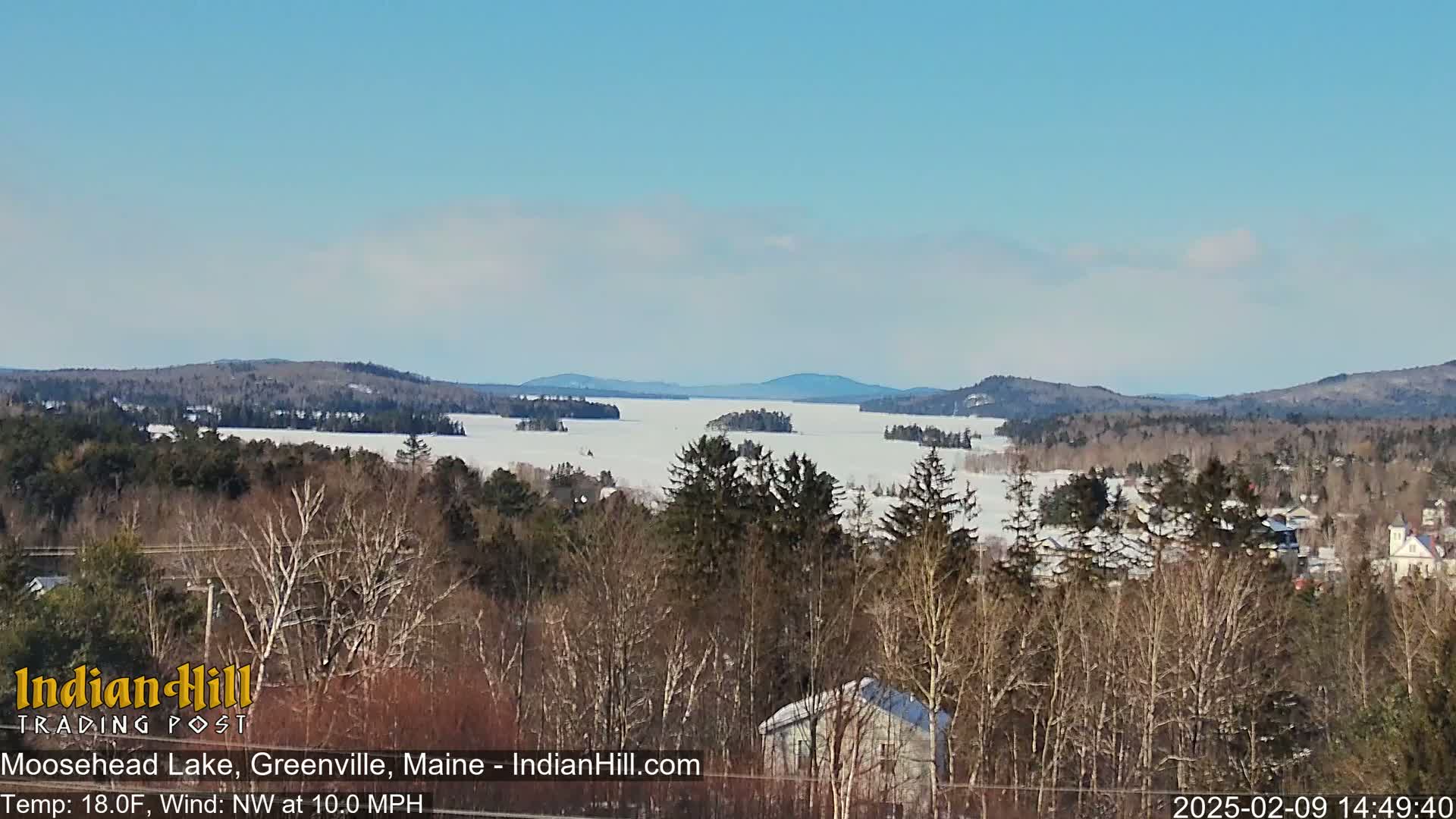 A snow-covered lake stretches to distant, snow-dusted hills under a clear, bright sky.