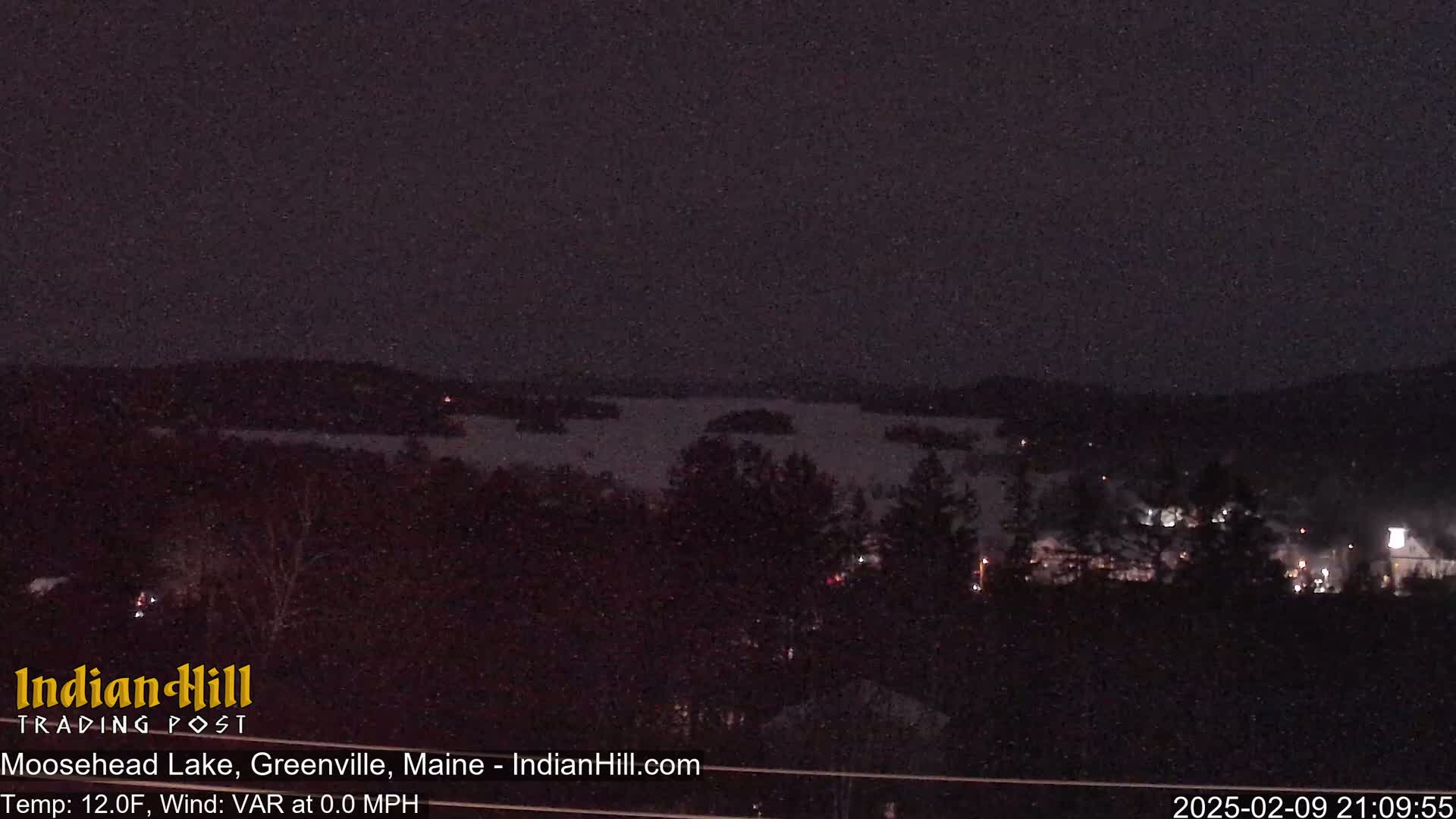 A nighttime view of a snow-covered lake and town under a dark, snowy sky.