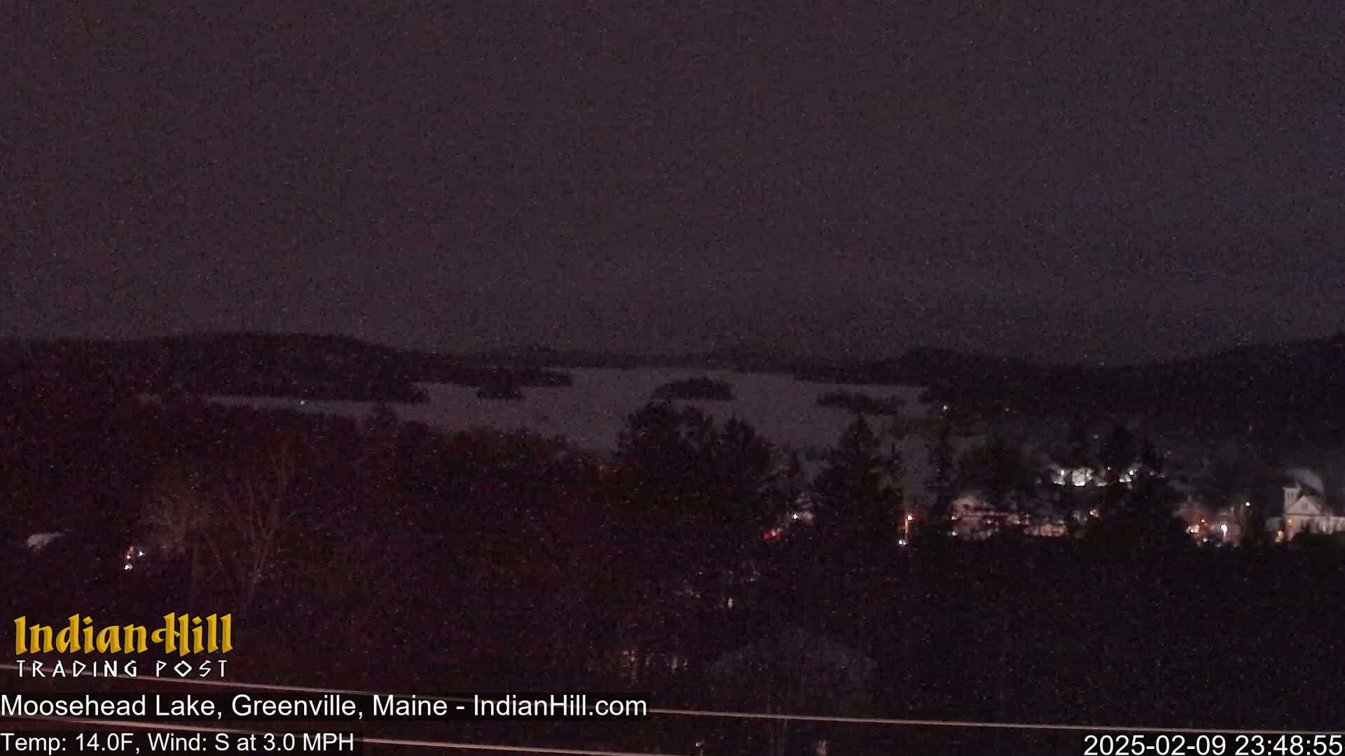 A nighttime view of a snow-covered lake and a town under a dark sky.