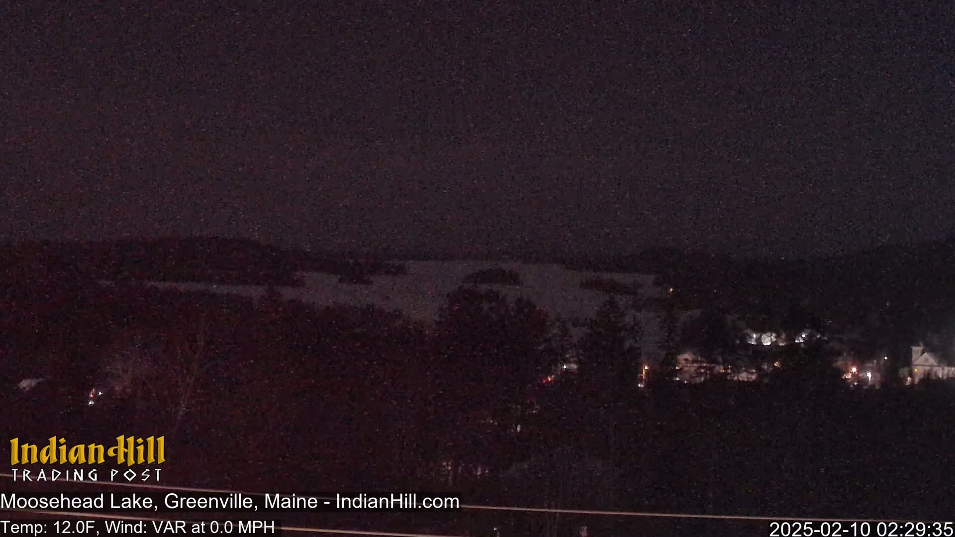 A nighttime view of a lake and dark, snow-covered landscape under a clear, dark sky.