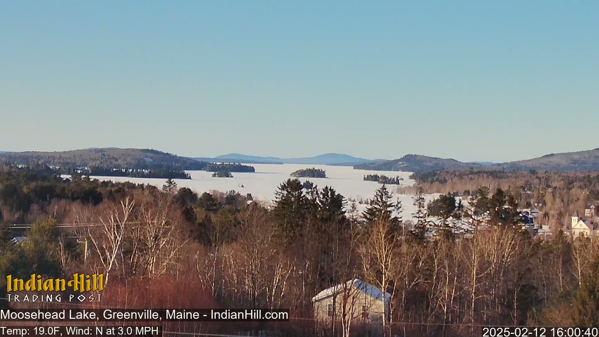A snow-covered frozen lake stretches to distant snow-dusted mountains under a clear blue sky.