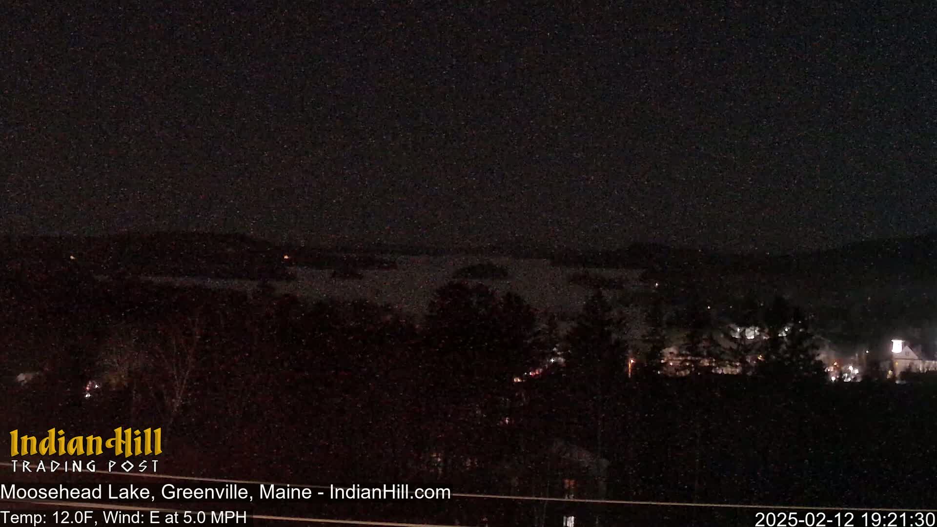 A nighttime view of a lake and dark, tree-covered land, under a clear, dark sky with a temperature of 12°F and an east wind at 5 mph.