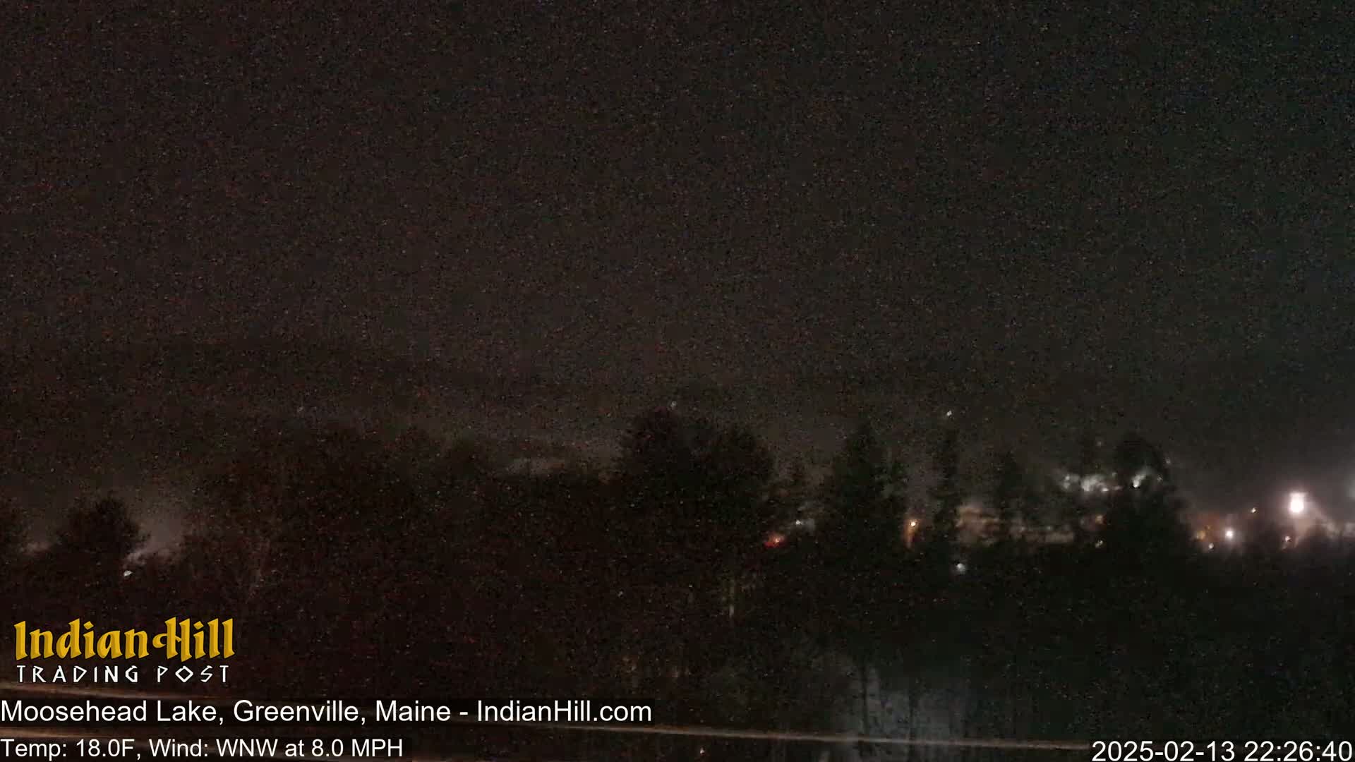 A nighttime long shot shows a dark, starlit sky over a line of dark trees under conditions of 18°F and a WNW wind at 8.0 mph.