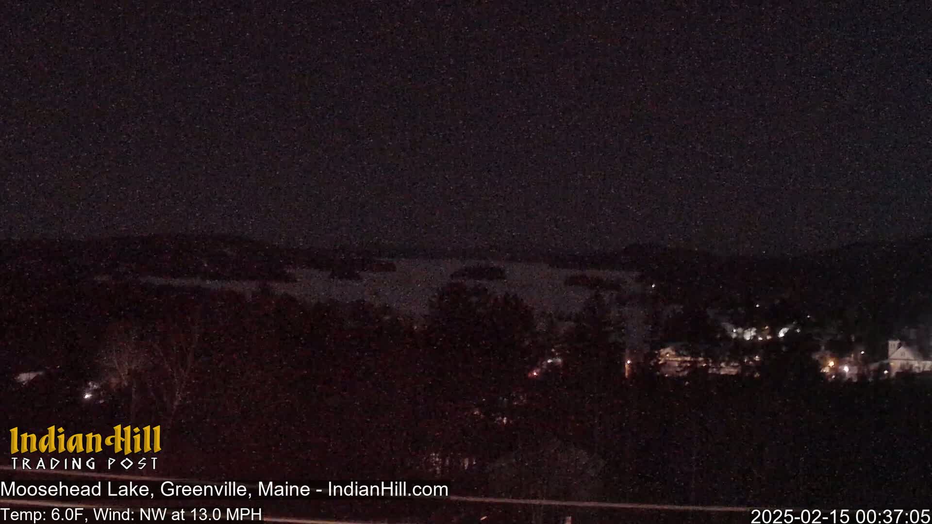 A nighttime view of a dark lake and a sparsely lit town under a clear, dark sky.
