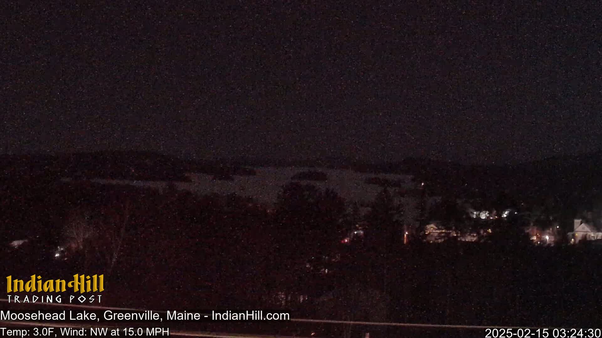 A nighttime view of a dark lake and trees under a clear, starry sky with a northwest wind at 15 mph and a temperature of 3 degrees Fahrenheit.