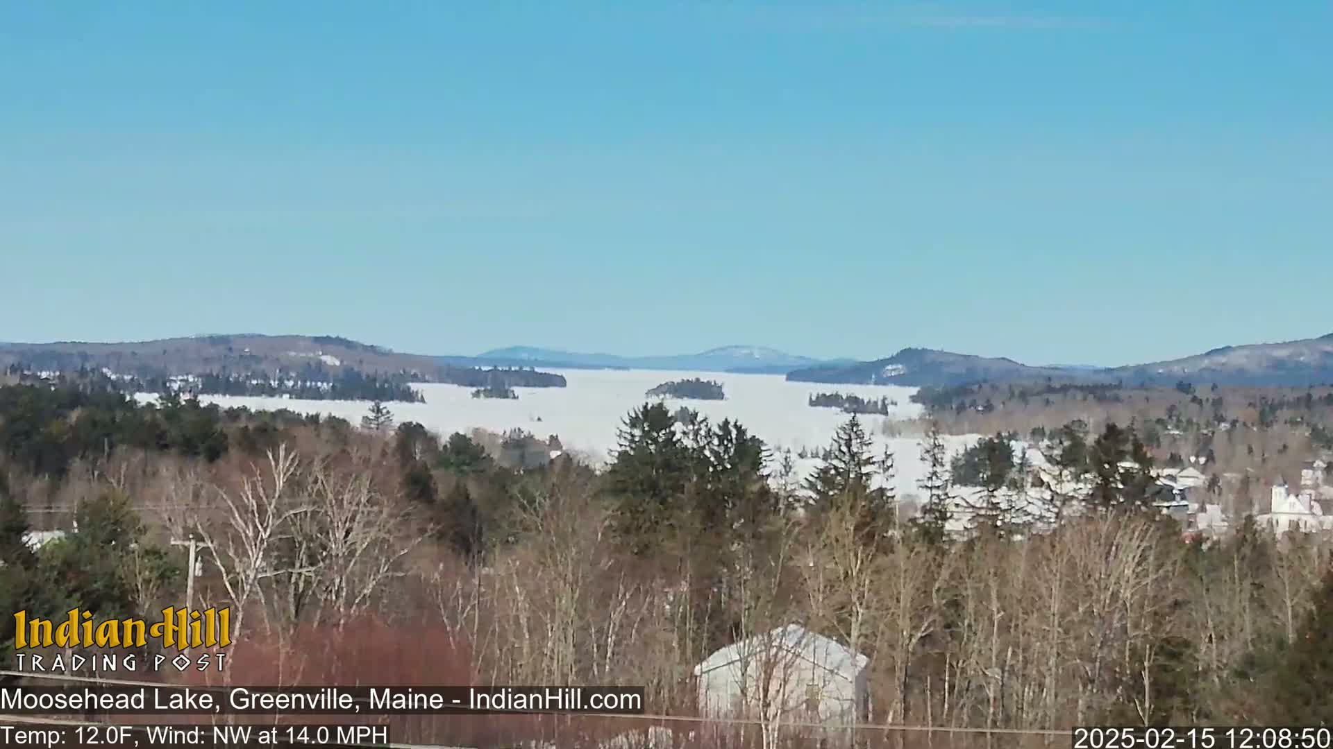A snow-covered lake is seen from a wooded hillside on a clear, cold, and windy day.
