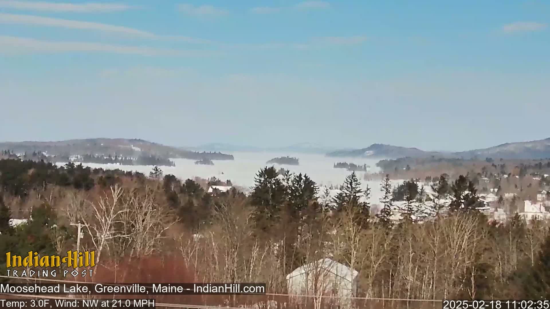 A snow-covered landscape reveals a lake shrouded in fog under a mostly clear sky.