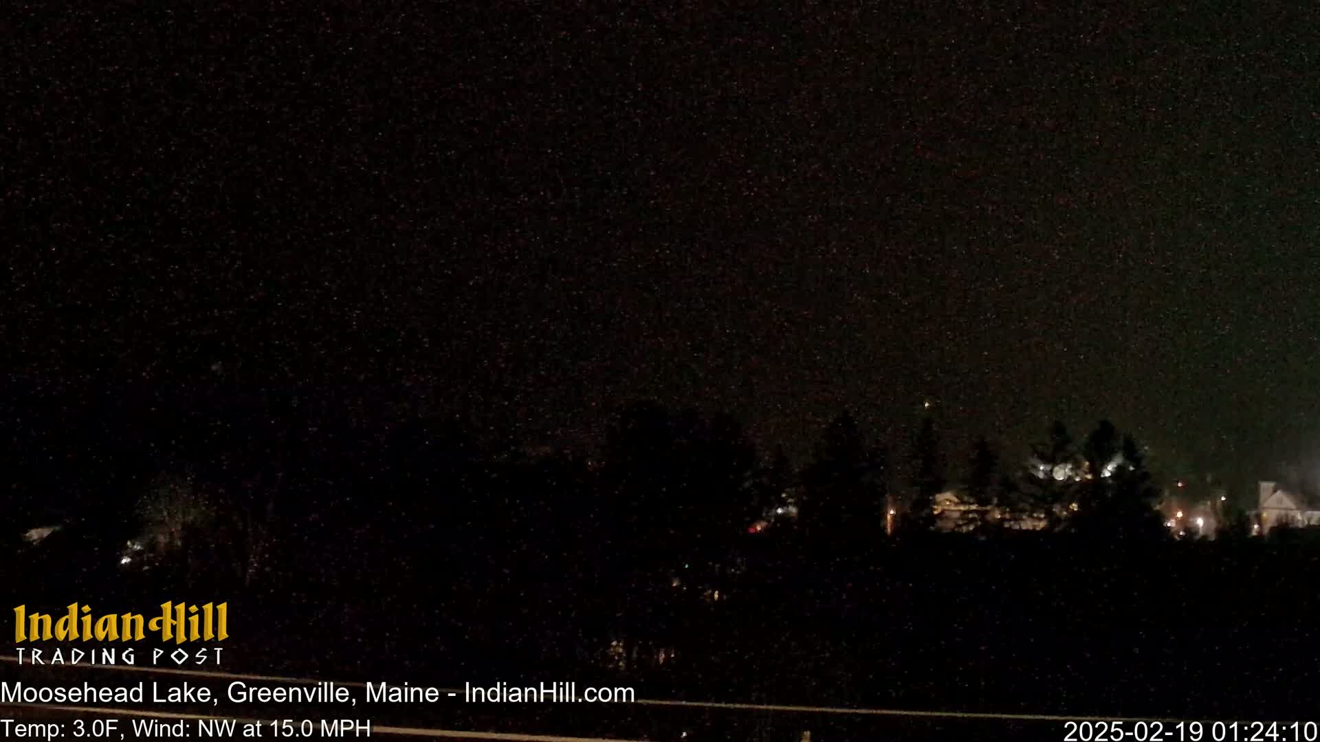 A nighttime view of a snow-covered landscape with a dark sky and faint lights in the distance, under conditions of 3°F and a 15 mph northwest wind.