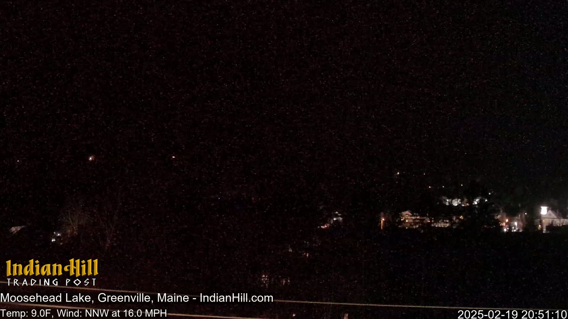 A nighttime long shot of a dimly lit town under a dark, clear sky with a northwest wind at 16 mph and a temperature of 9°F.