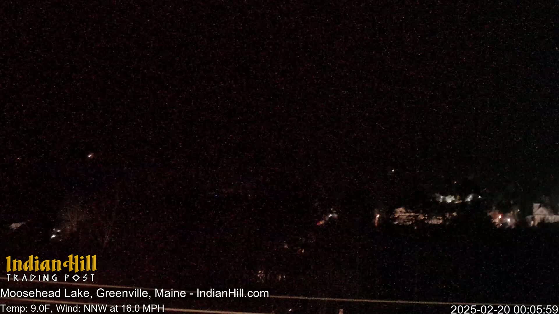A nighttime long shot of dimly lit buildings and trees under a dark, possibly snowy sky.