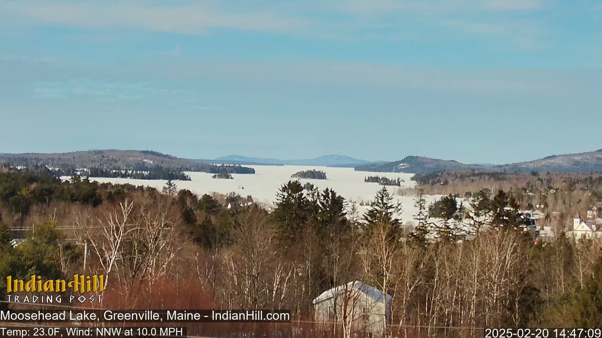 A snow-covered lake stretches to distant, snow-dusted mountains under a clear blue sky.