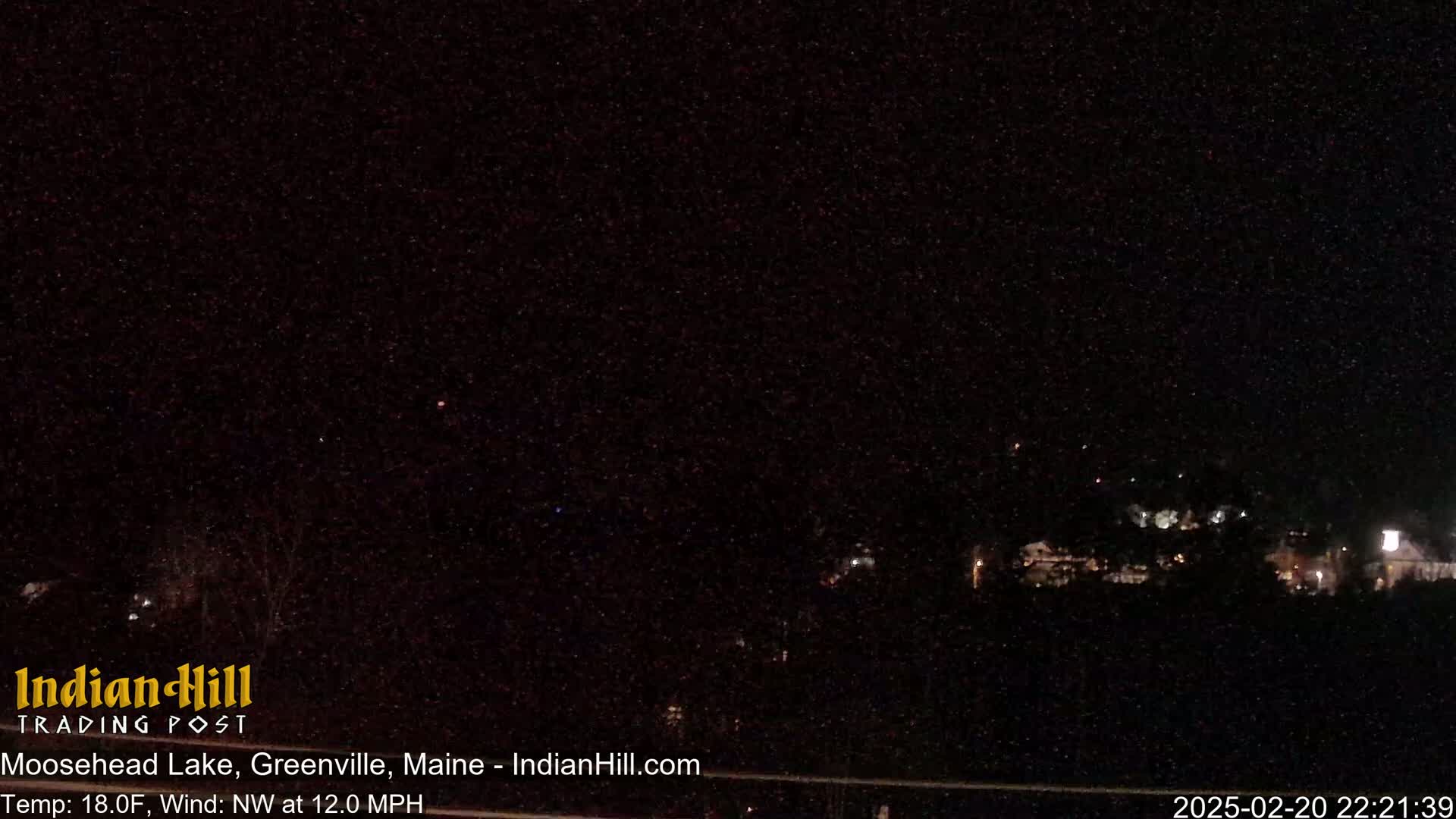 A nighttime long shot of a dark landscape with a few distant lights and a northwest wind at 12 mph, and a temperature of 18 degrees Fahrenheit.