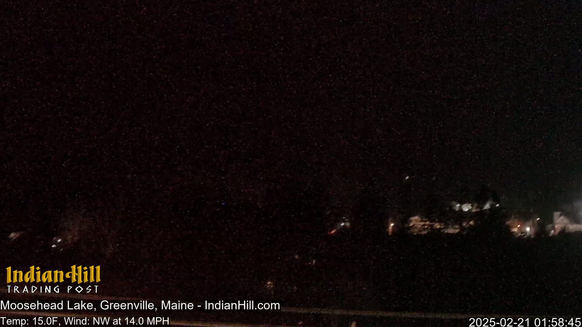 A nighttime long shot of a dark landscape with a few distant lights under a clear, dark sky.