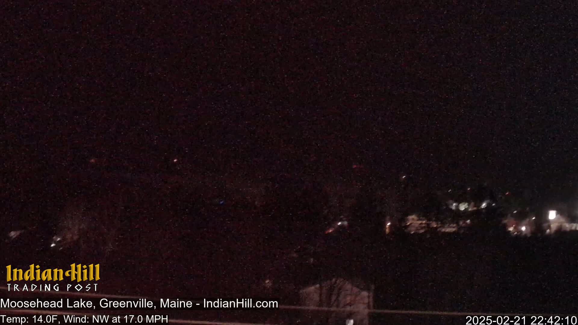 A nighttime long shot of sparsely lit buildings and trees under a dark, clear sky with a northwest wind.
